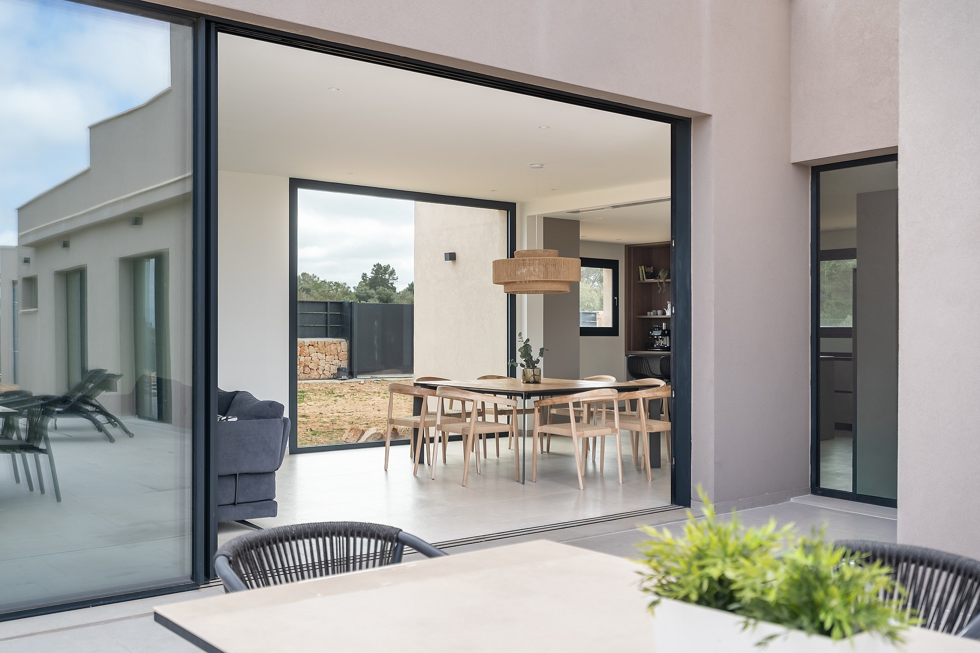 View from a terrace into an open-plan dining room with a wooden table, chairs, and large sliding glass doors.