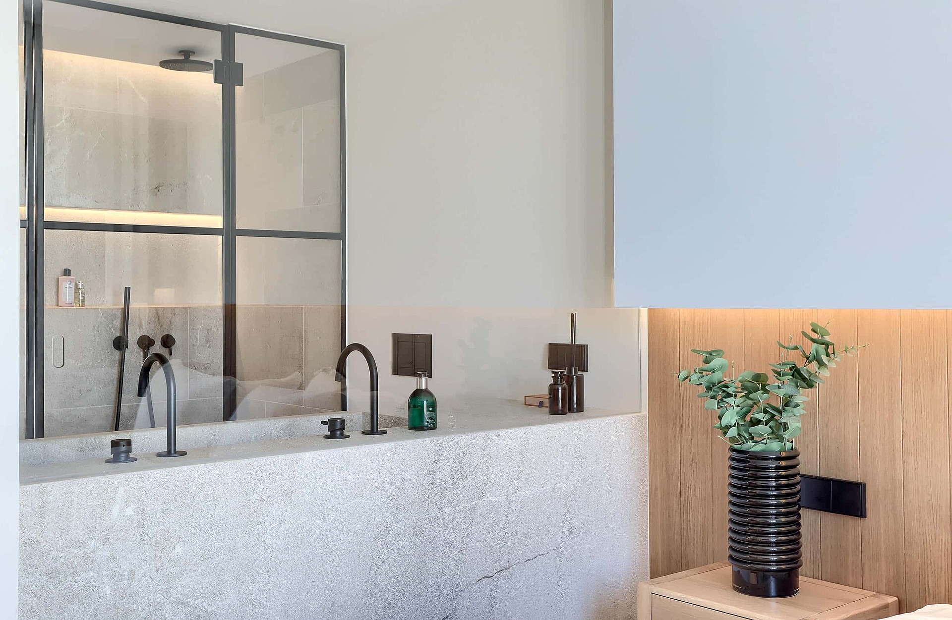 Close up of a bathroom vanity with terrazzo countertop, black metal-framed glass shower partition, and vertical wood wall paneling.