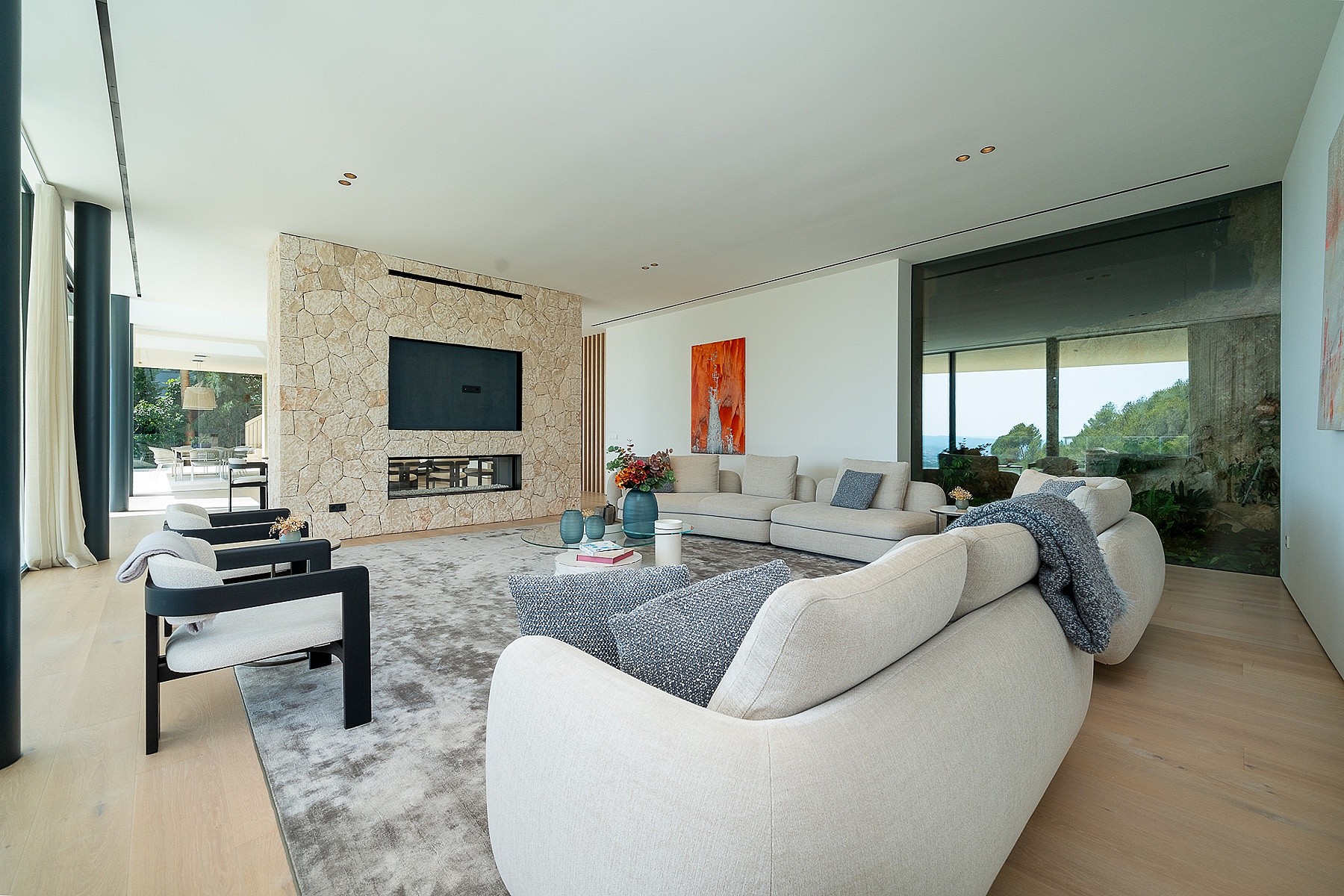Spacious living room featuring a floor-to-ceiling natural stone wall with a fireplace, light wood flooring, and modern furniture.