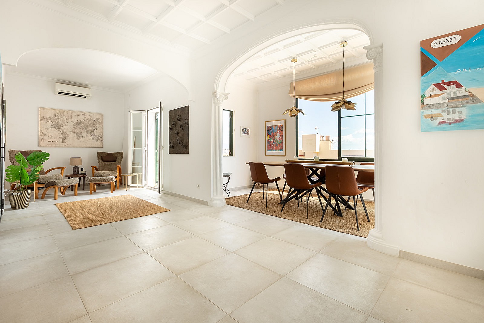 A bright living and dining room with white arched walls, tiled floors, a wooden dining set, and a cozy seating area.