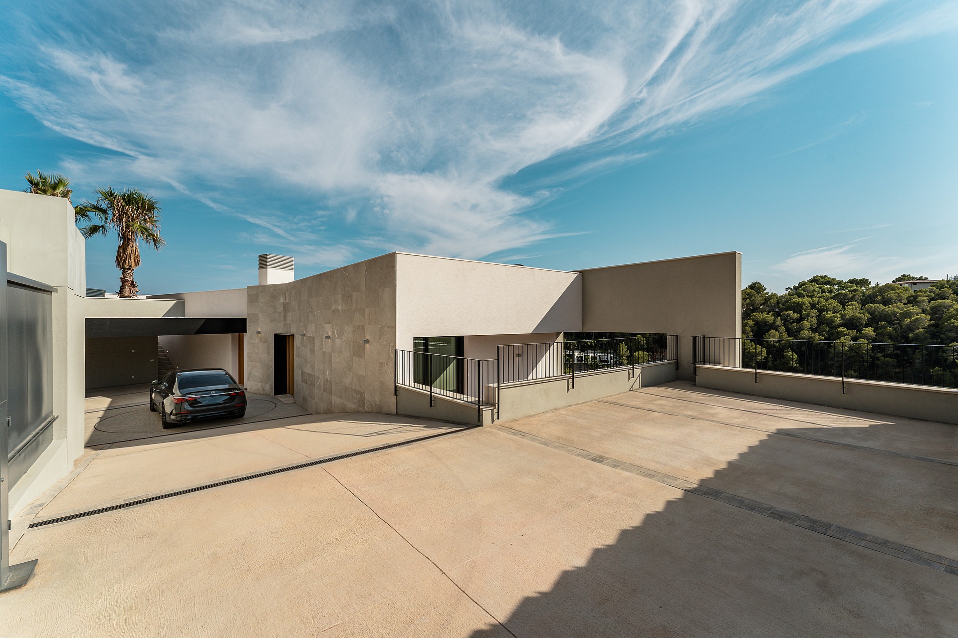 Wide view of a contemporary house exterior with a paved entrance, covered parking area, and light-toned masonry walls.