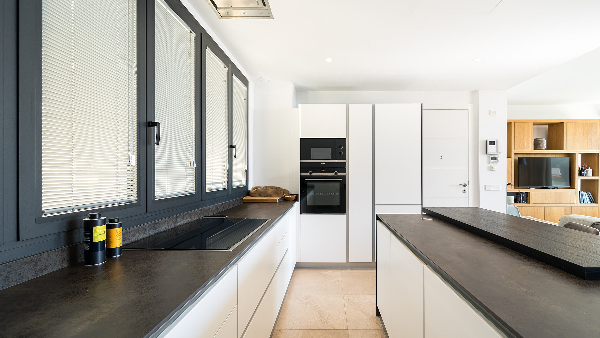 Modern kitchen featuring dark matte counters, white cabinetry, and large windows with integrated blinds.