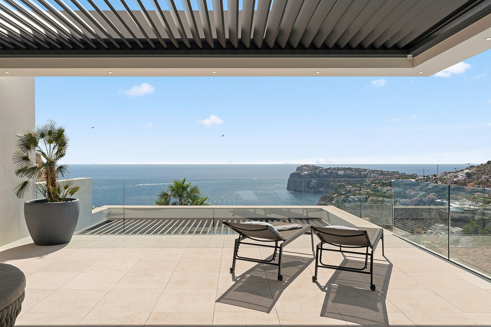 A covered terrace with two sun loungers facing the sea in Port d'Andratx, featuring a glass railing and a louvered pergola.