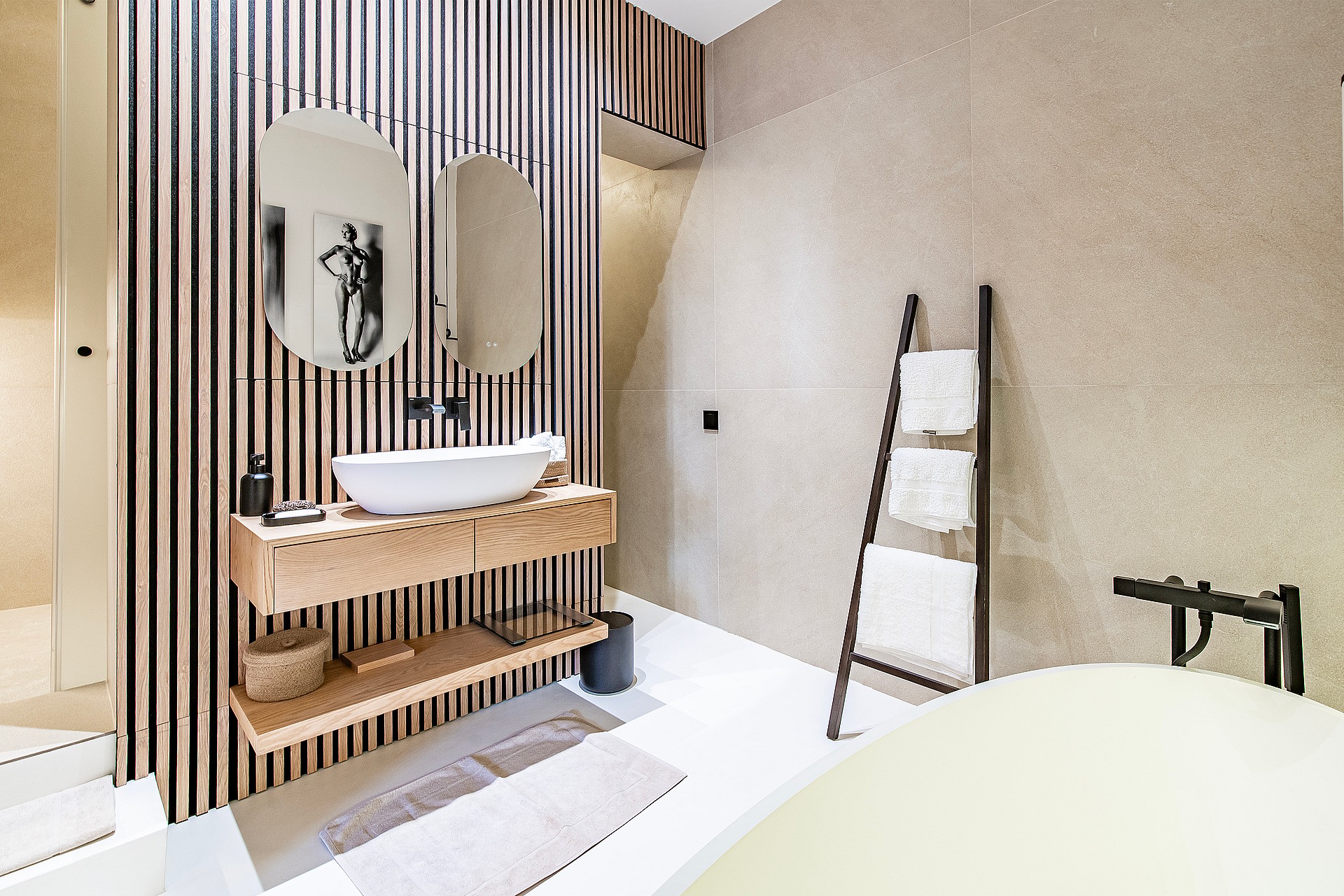 Bathroom interior featuring a white vessel sink on a wooden floating vanity, oval mirrors, and a decorative ladder towel rack.
