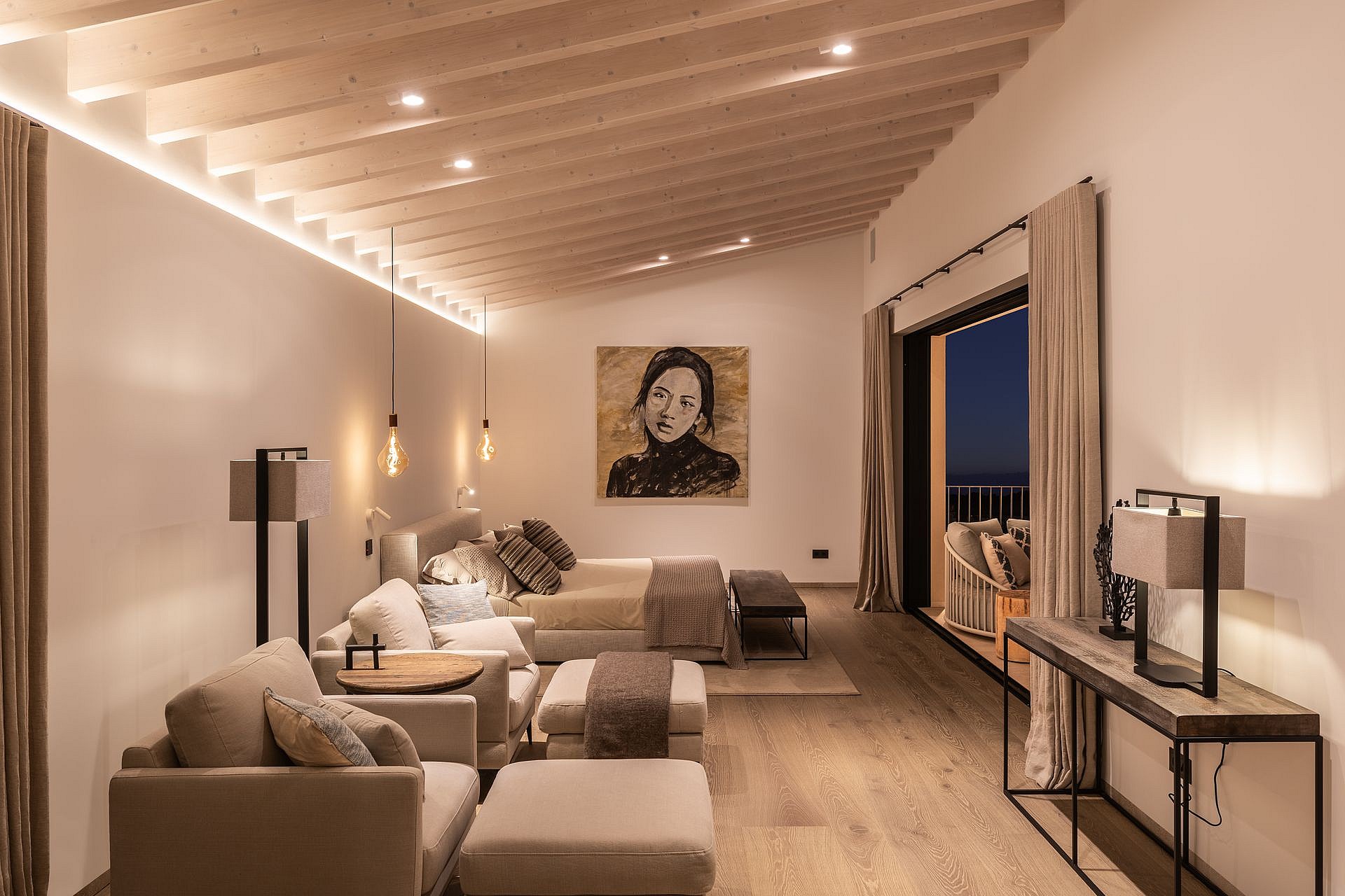 Spacious bedroom with a king-sized bed, seating area, and sliding glass doors opening to a terrace at dusk.