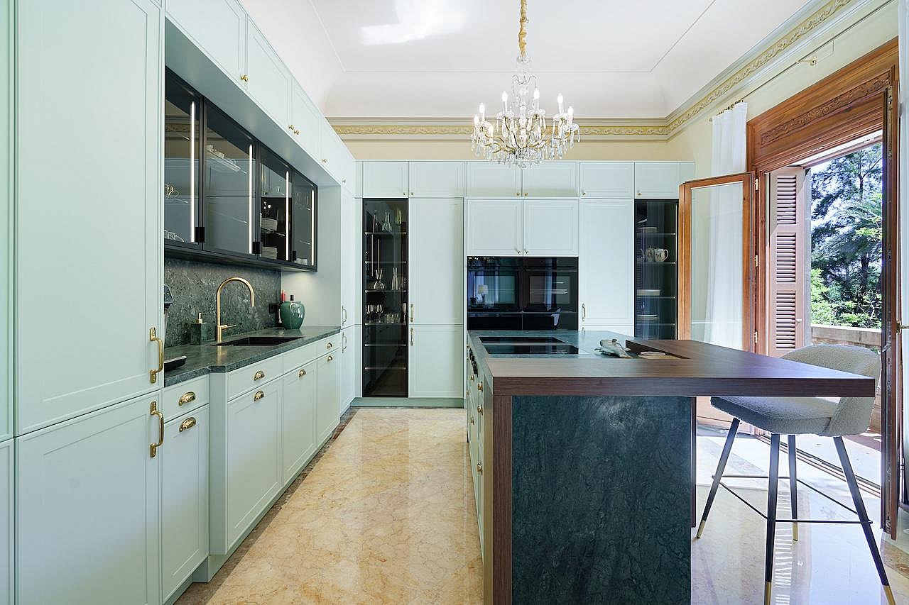 Modern kitchen with light green cabinetry, a dark marble kitchen island, a crystal chandelier, and balcony doors.