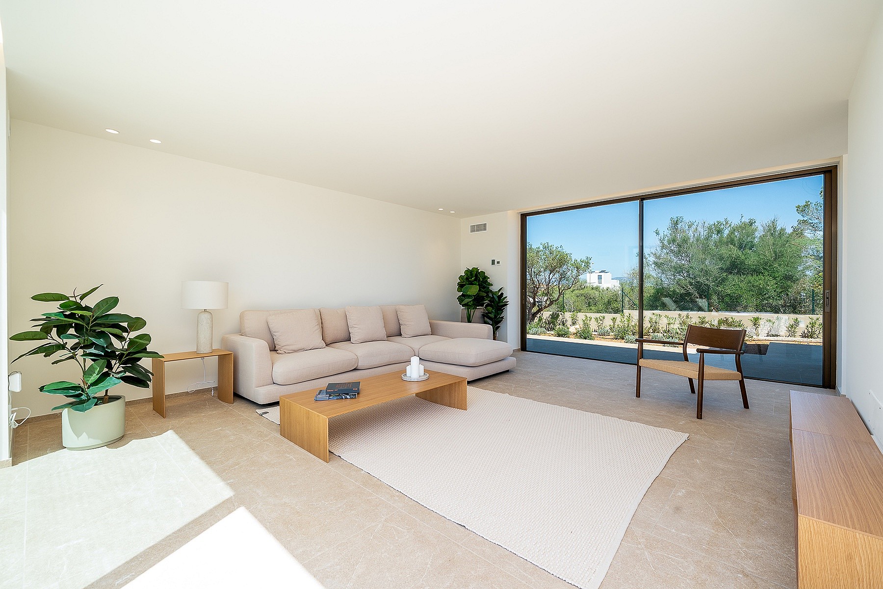 Modern living room featuring a beige sectional sofa, low wooden coffee table, and large sliding glass doors opening to a garden.