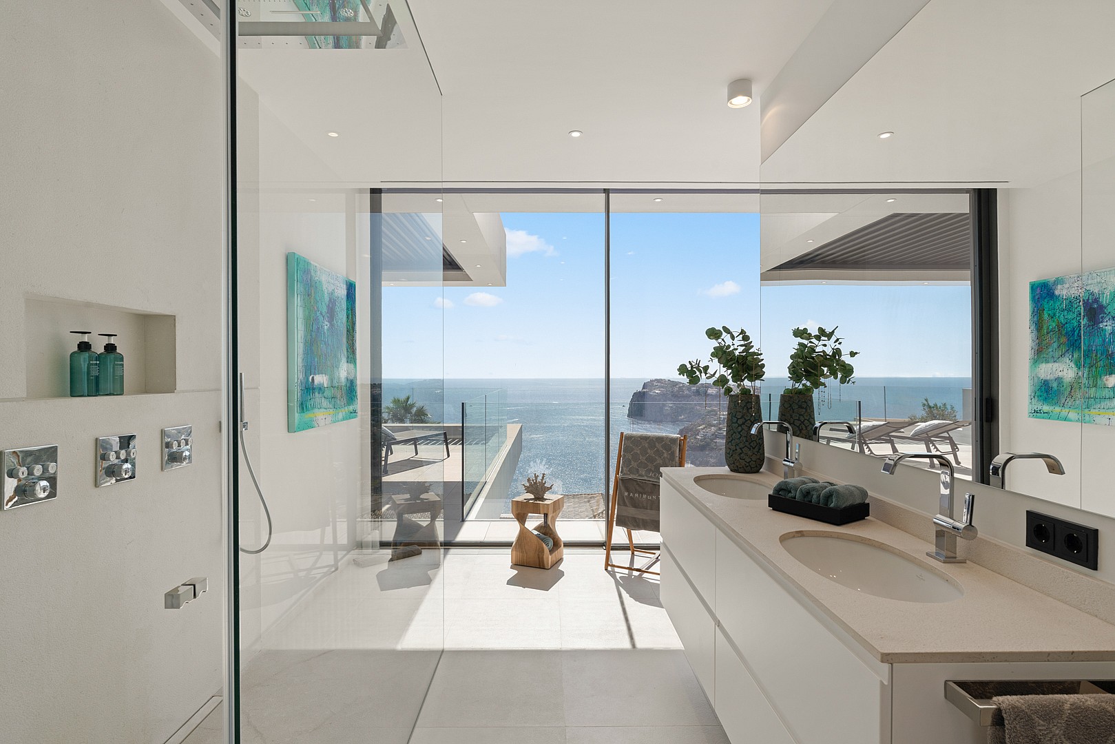 Modern bathroom featuring a double vanity, glass-enclosed shower, and floor-to-ceiling windows overlooking the ocean.