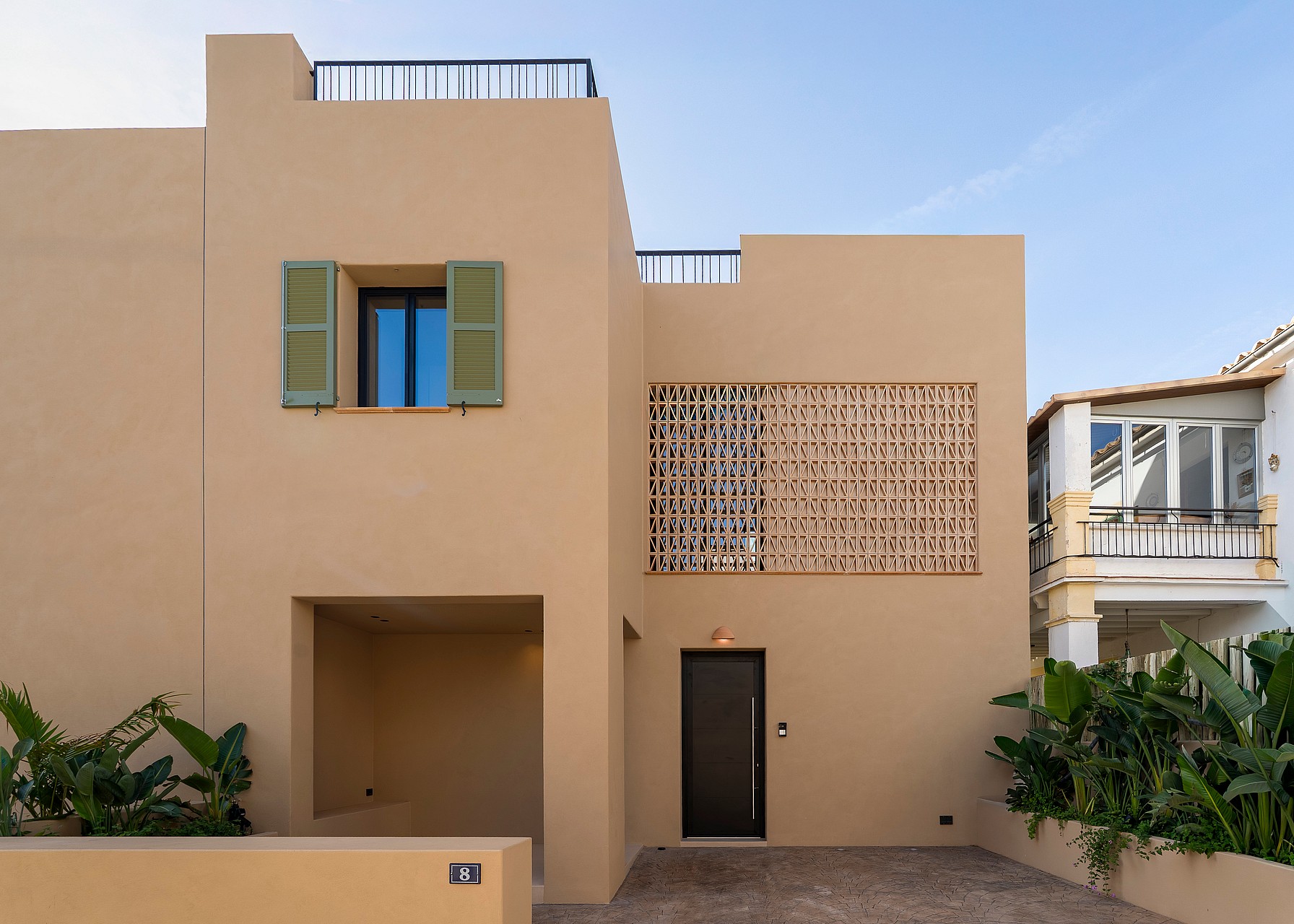 Two-story townhouse exterior with beige stucco walls, green window shutters, and a terracotta lattice screen by the entrance.