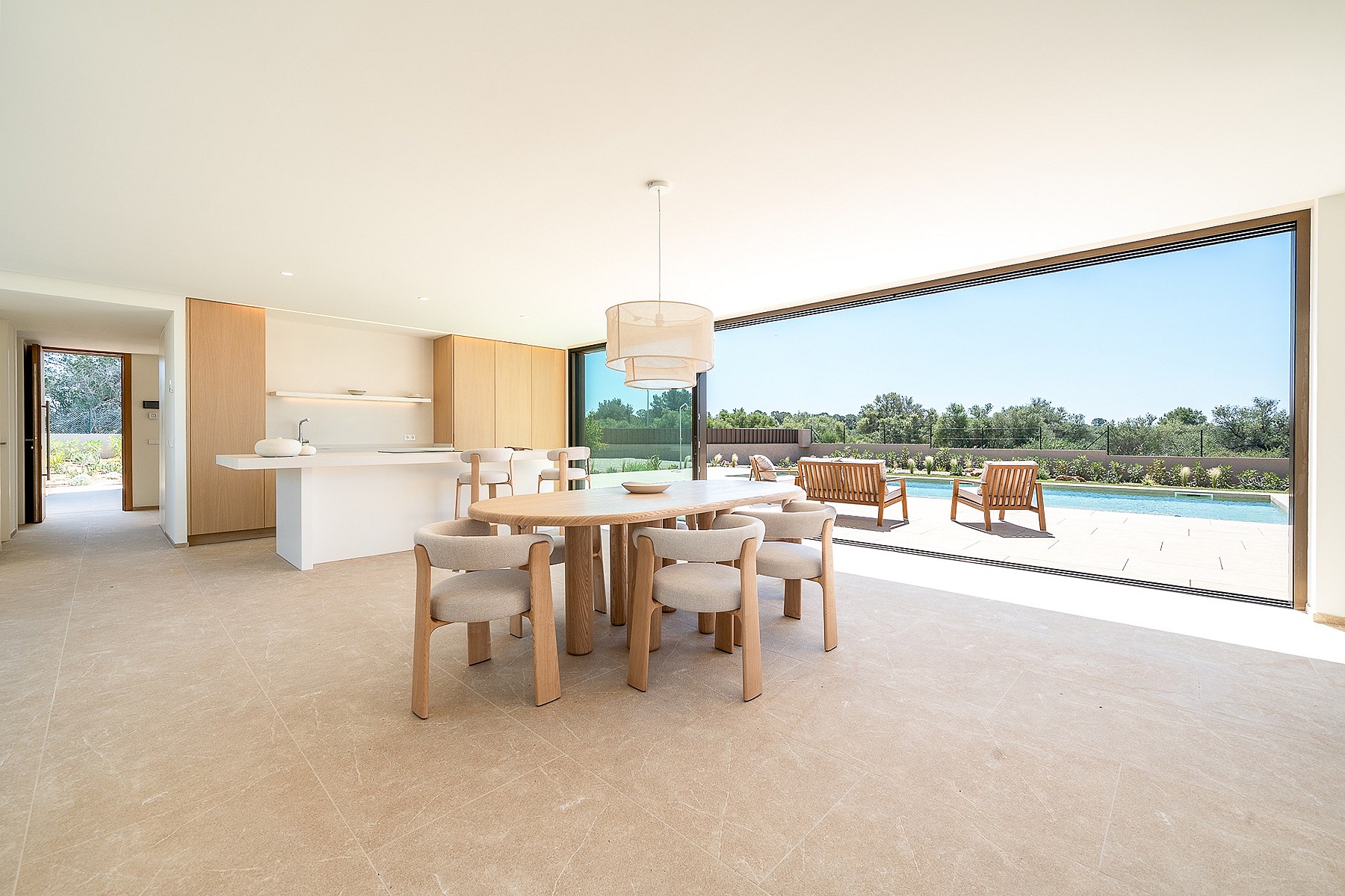 Bright dining area with oval wooden table and cream upholstered chairs, large sliding doors opening to an outdoor pool deck.