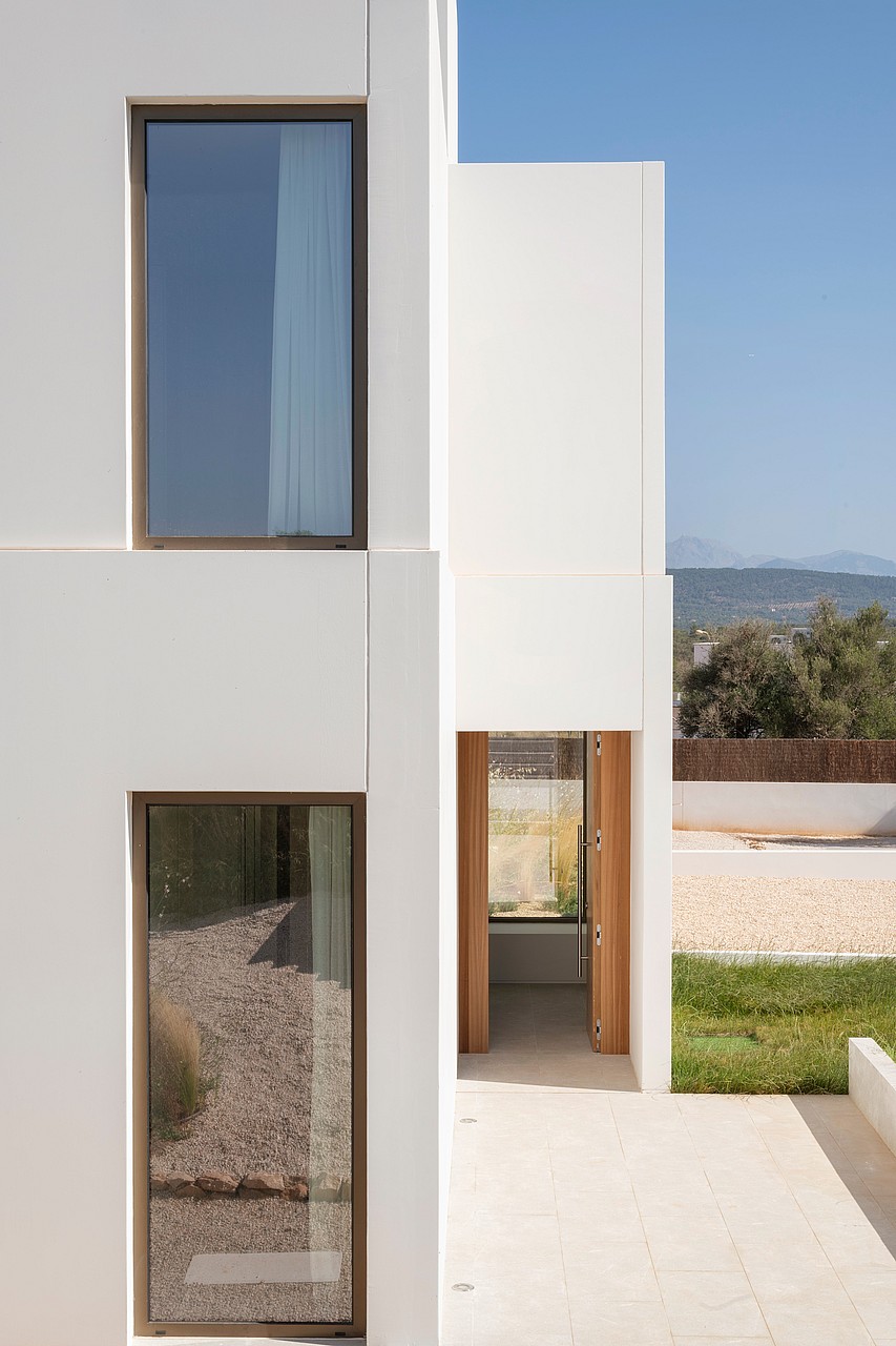 A white modern building exterior featuring clean geometric lines, large windows, and a wooden entryway with mountain views.
