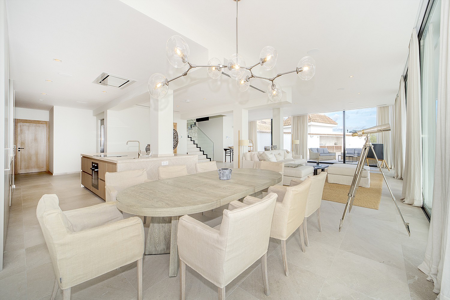 Bright open-plan space featuring an oval dining table, contemporary chandelier, and kitchen island with oak cabinetry.