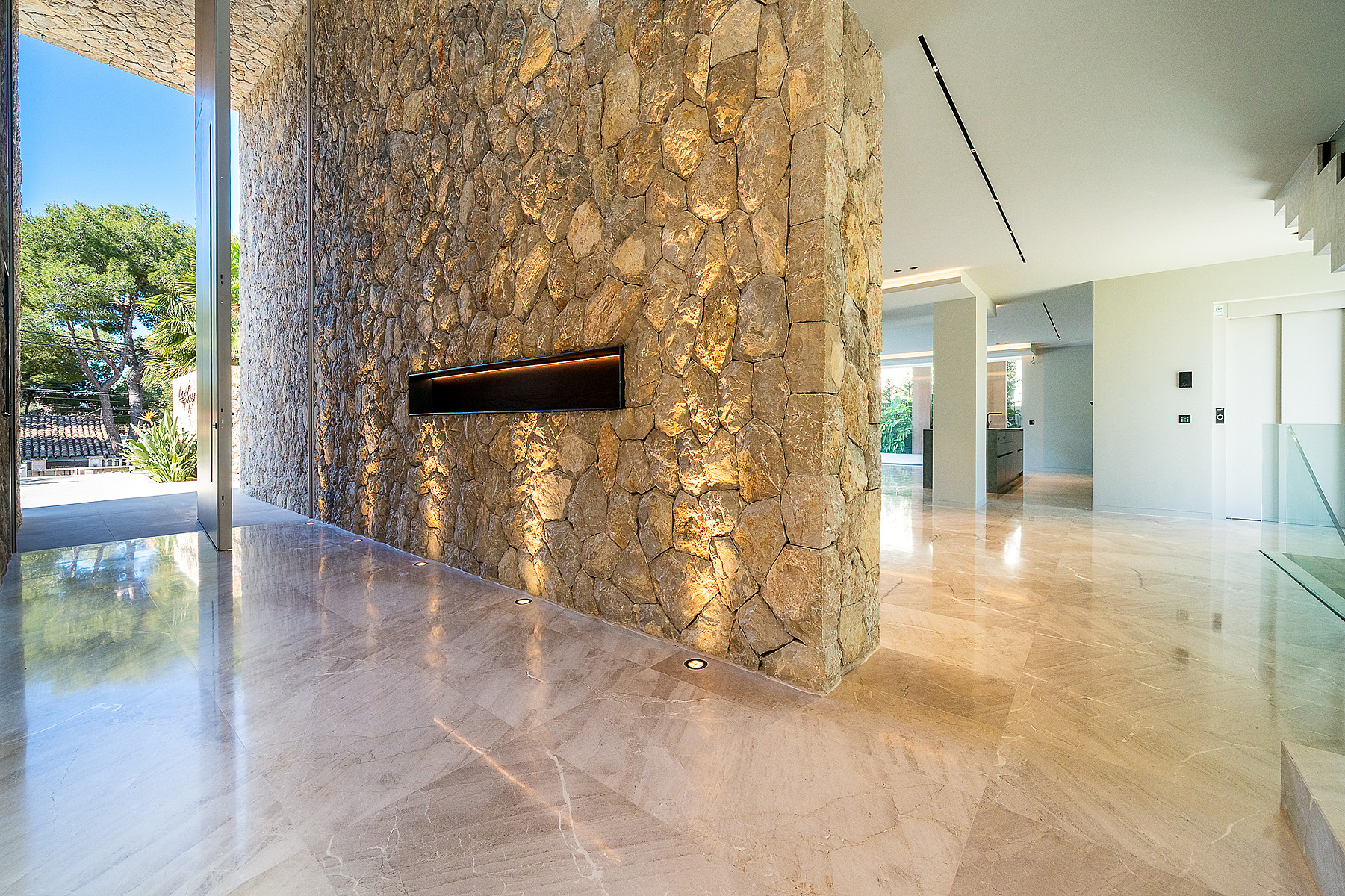 Interior entrance hall featuring a large natural stone wall with an integrated horizontal fireplace, polished stone floors, and recessed lighting.