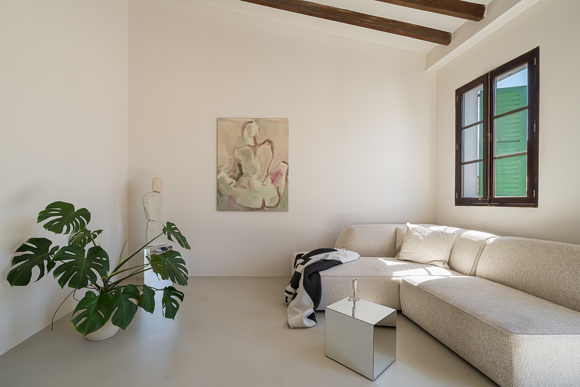 Minimalist living area featuring microcement flooring, light textured sofa, exposed timber beams and a large potted plant.