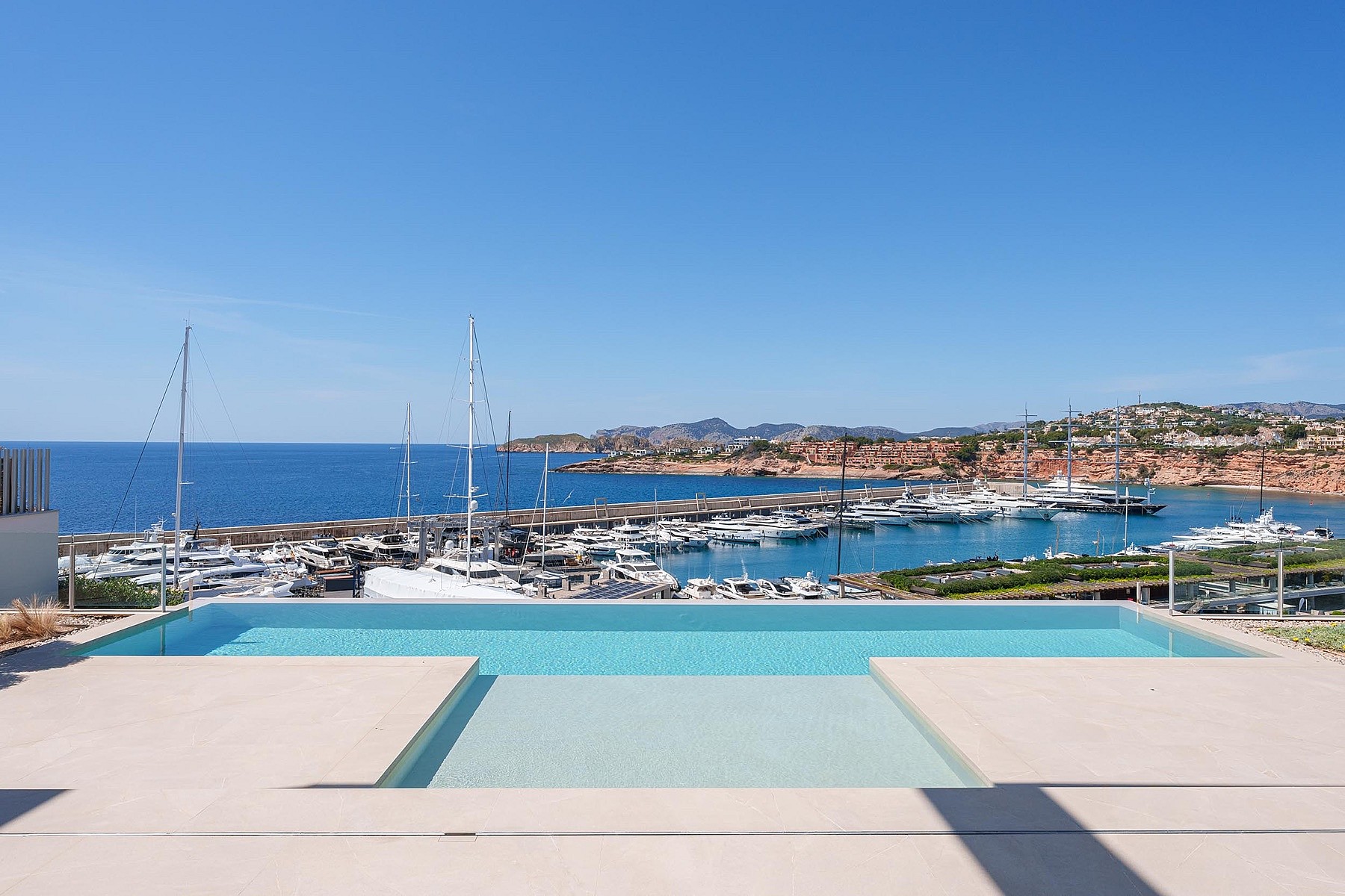 A rectangular infinity pool with turquoise water in the foreground, framing a direct view of the marina and yachts.