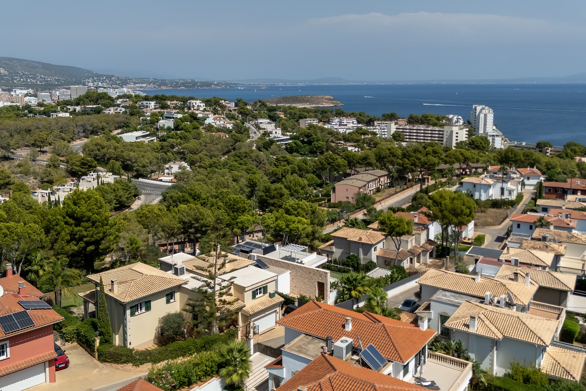 High-angle aerial photograph of the coastal residential neighborhood in Cala Vinyes, showing Mediterranean villas with terracotta roofs set among pine trees and sea views.