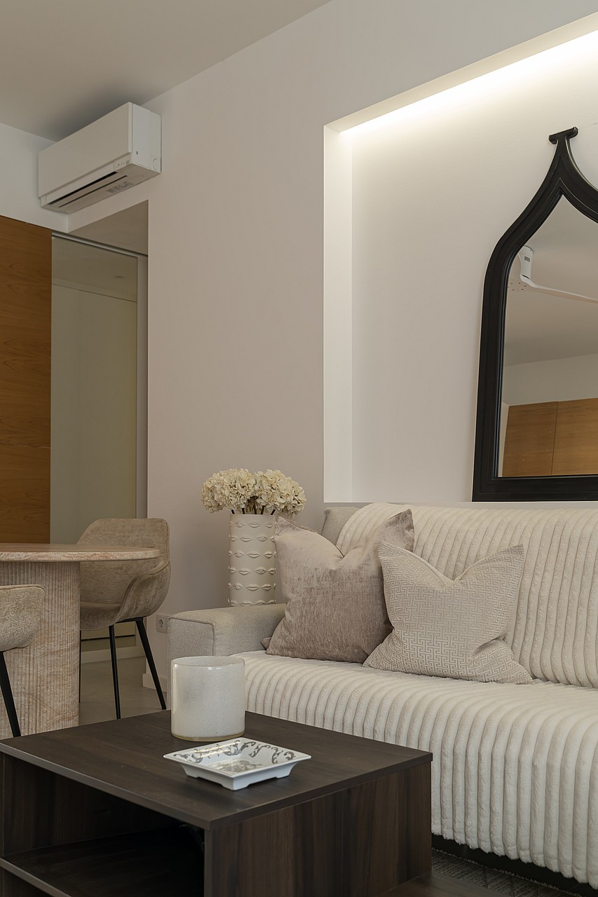 A modern living area featuring a ribbed beige sofa, dark wood coffee table, and an arched black-framed wall mirror.