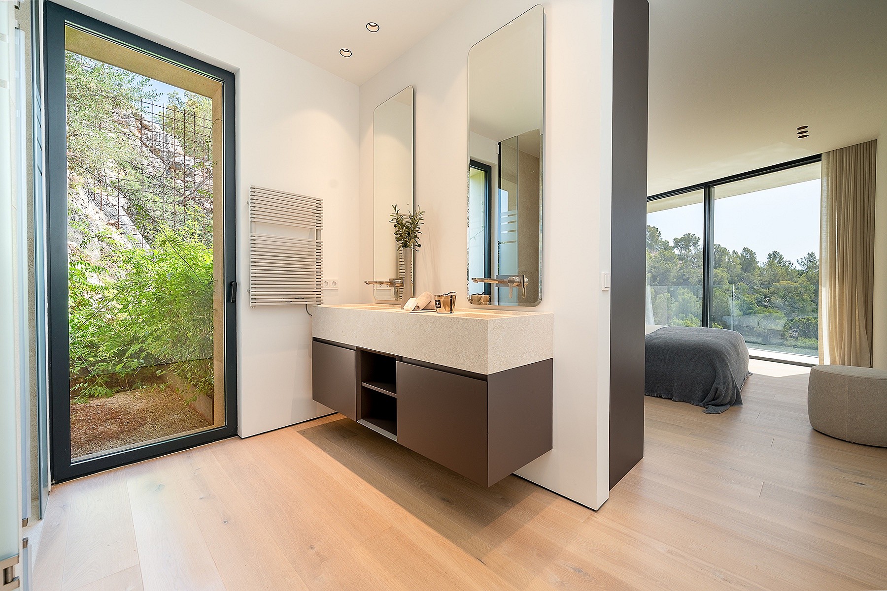 Modern master bathroom with a floating vanity, light oak flooring, and a glass door opening to a private garden area.