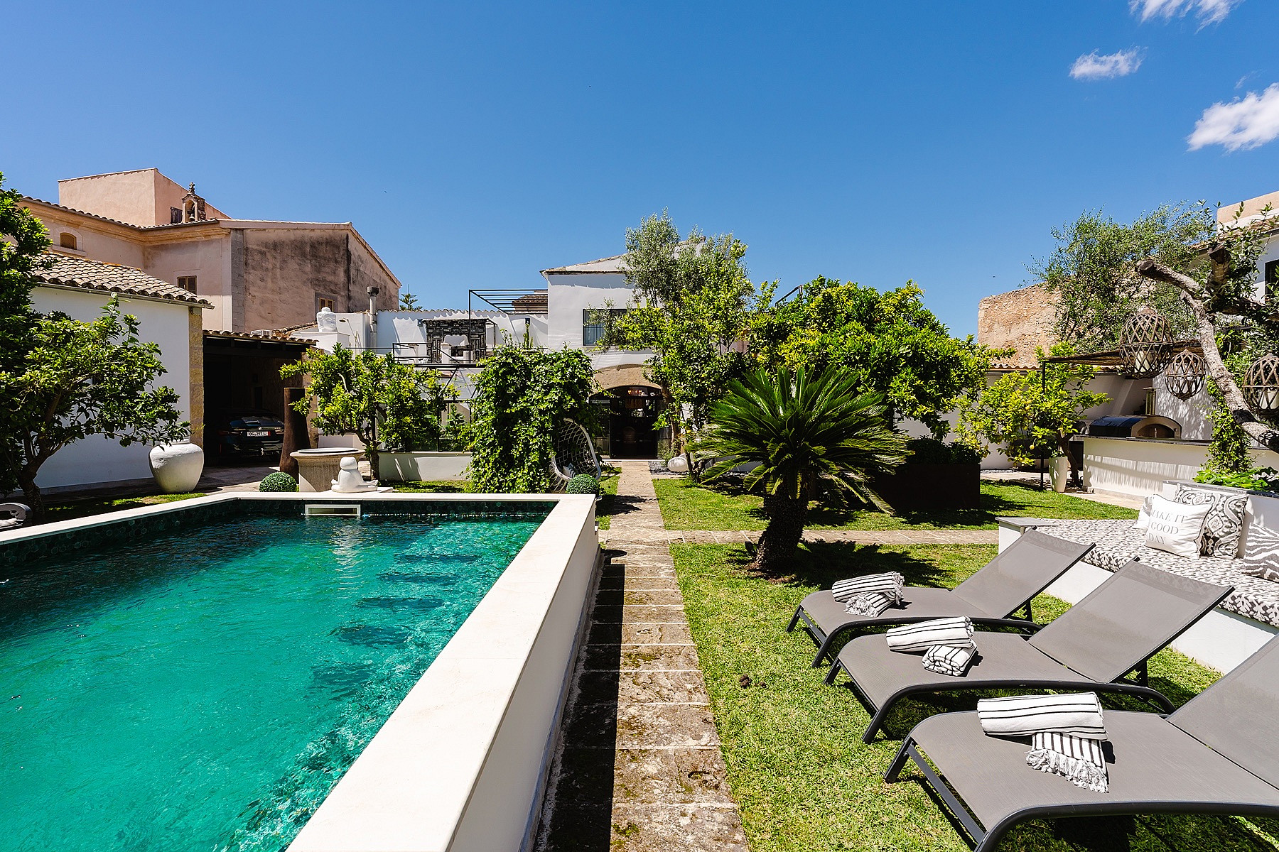 A rectangular swimming pool with turquoise water bordered by a stone path and a grassy lawn with three sun loungers.