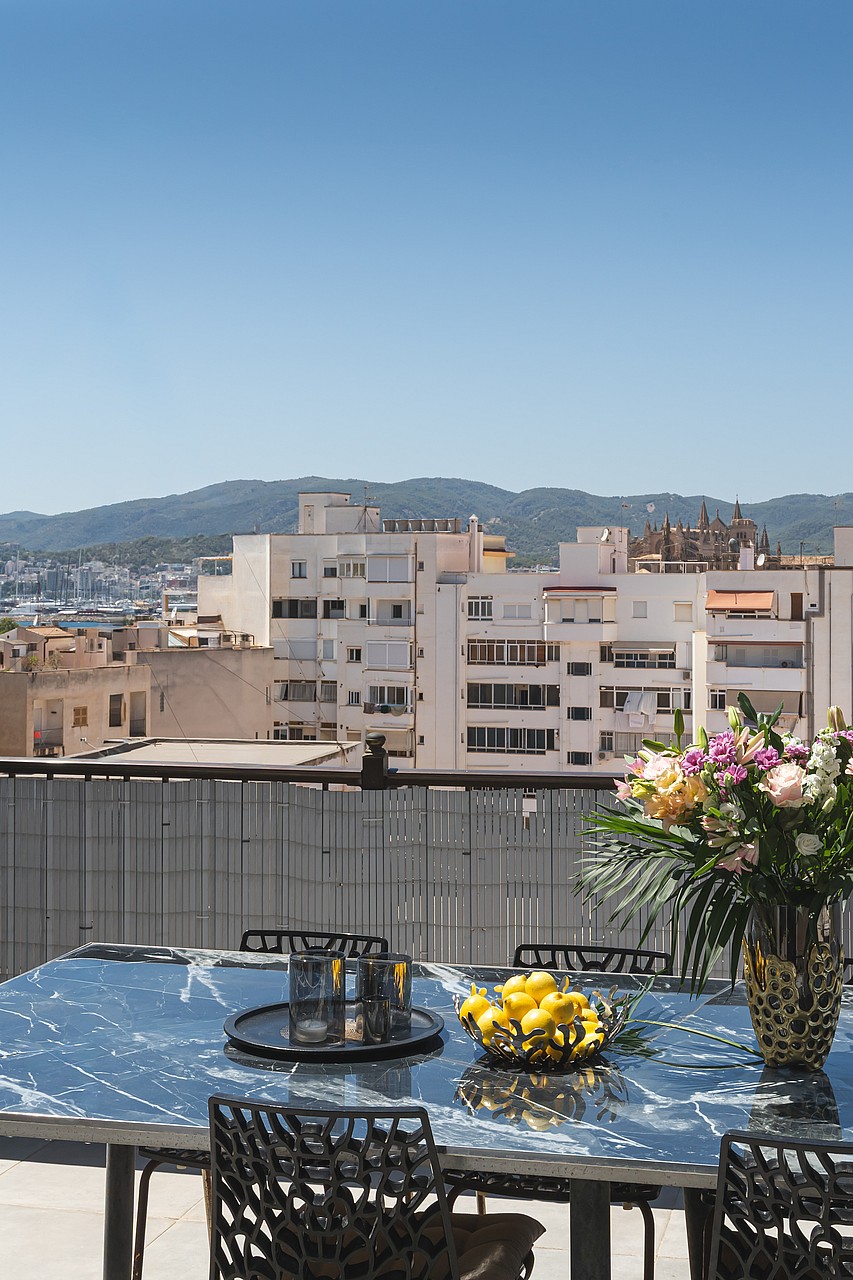 An outdoor terrace table set with a floral arrangement, overlooking a dense urban cityscape with mountains in the background.