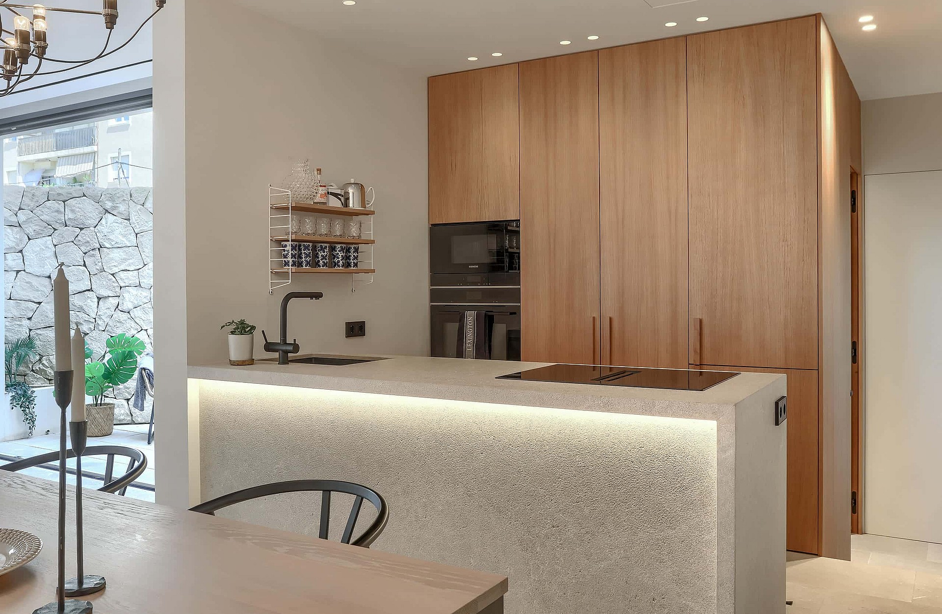 Contemporary kitchen featuring a terrazzo island with integrated under-counter lighting, wooden cabinetry, and dining area.