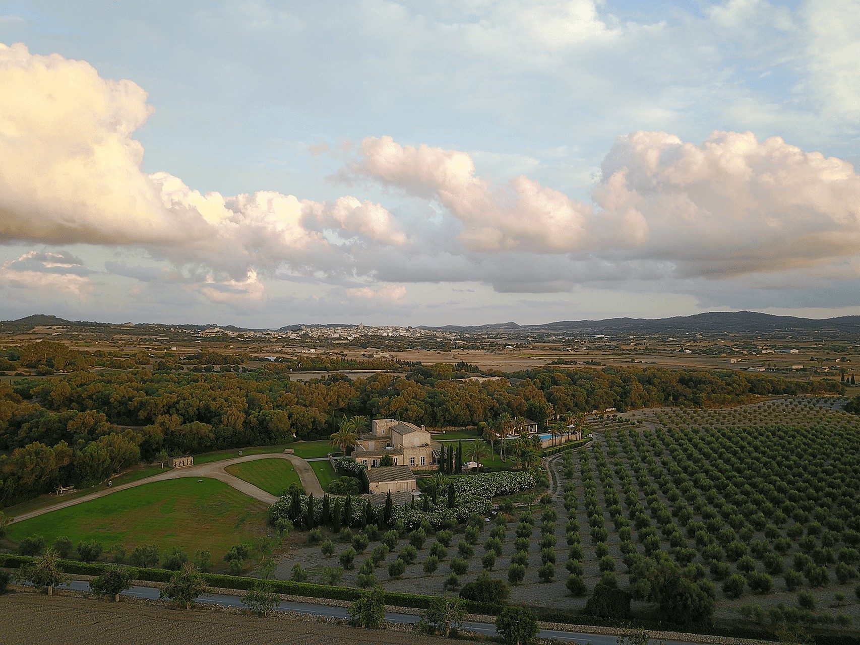 High-angle aerial photograph of a stone finca surrounded by olive groves and open fields in Algaida under a cloudy sky.