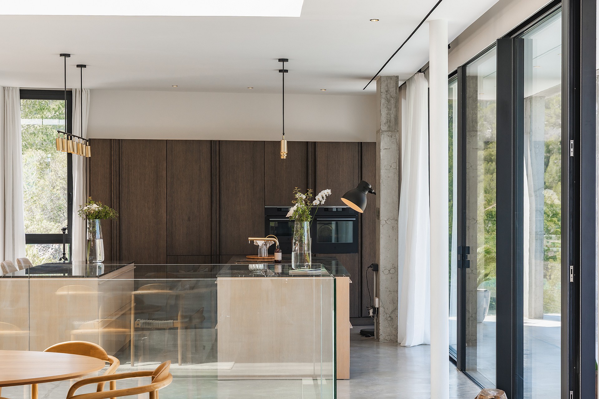 Modern kitchen featuring a central island, dark wood wall units, and floor-to-ceiling windows in a bright interior.