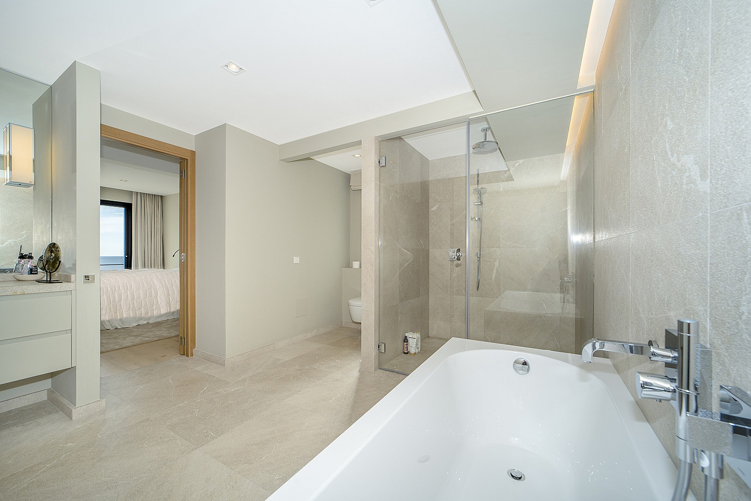Modern master bathroom featuring a white soaking tub, walk-in glass shower, and neutral stone tiling with open layout.