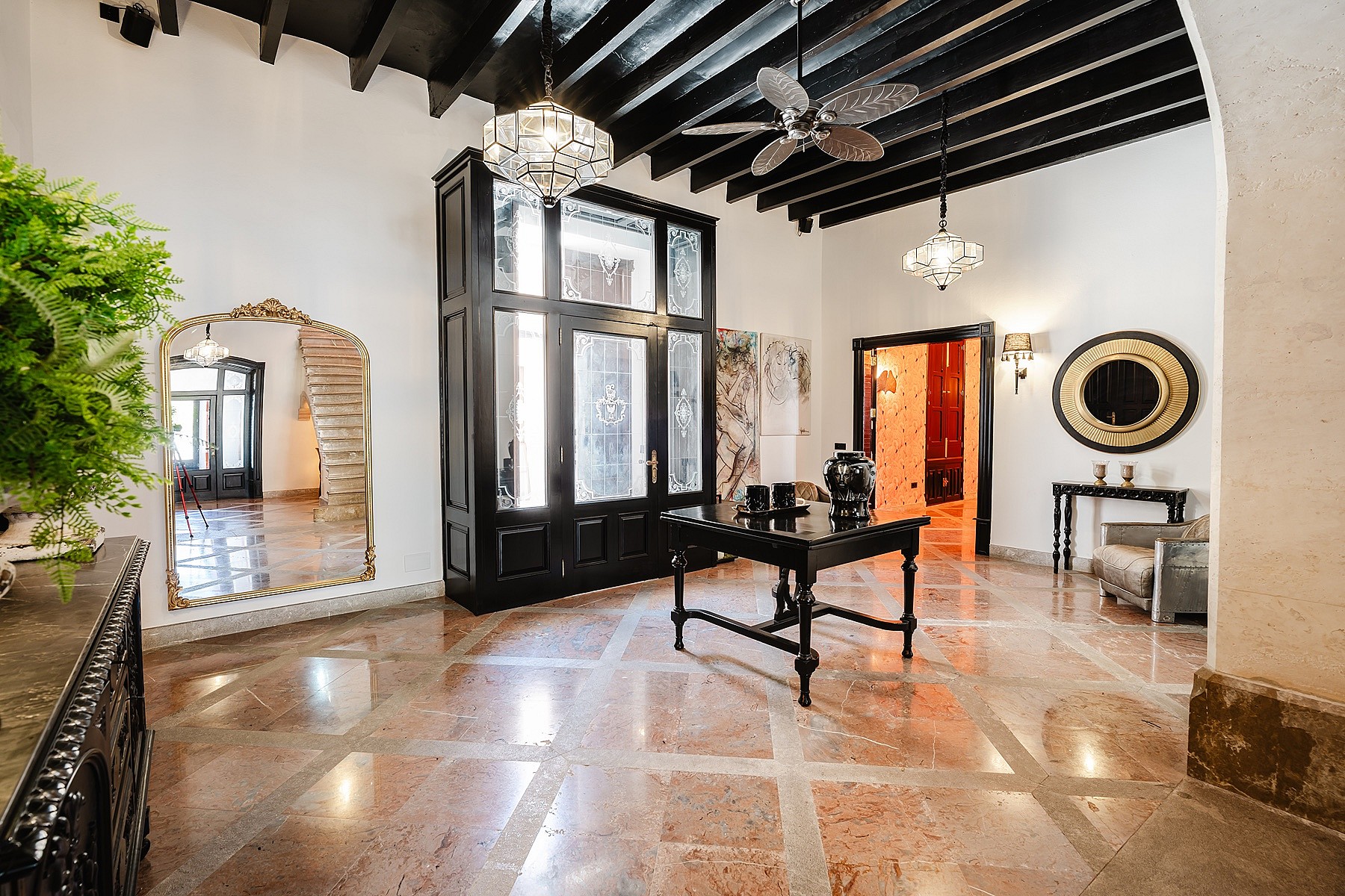A spacious entrance hall in a townhouse featuring polished stone floors, dark wood beamed ceilings, and an ornate black frame partition.