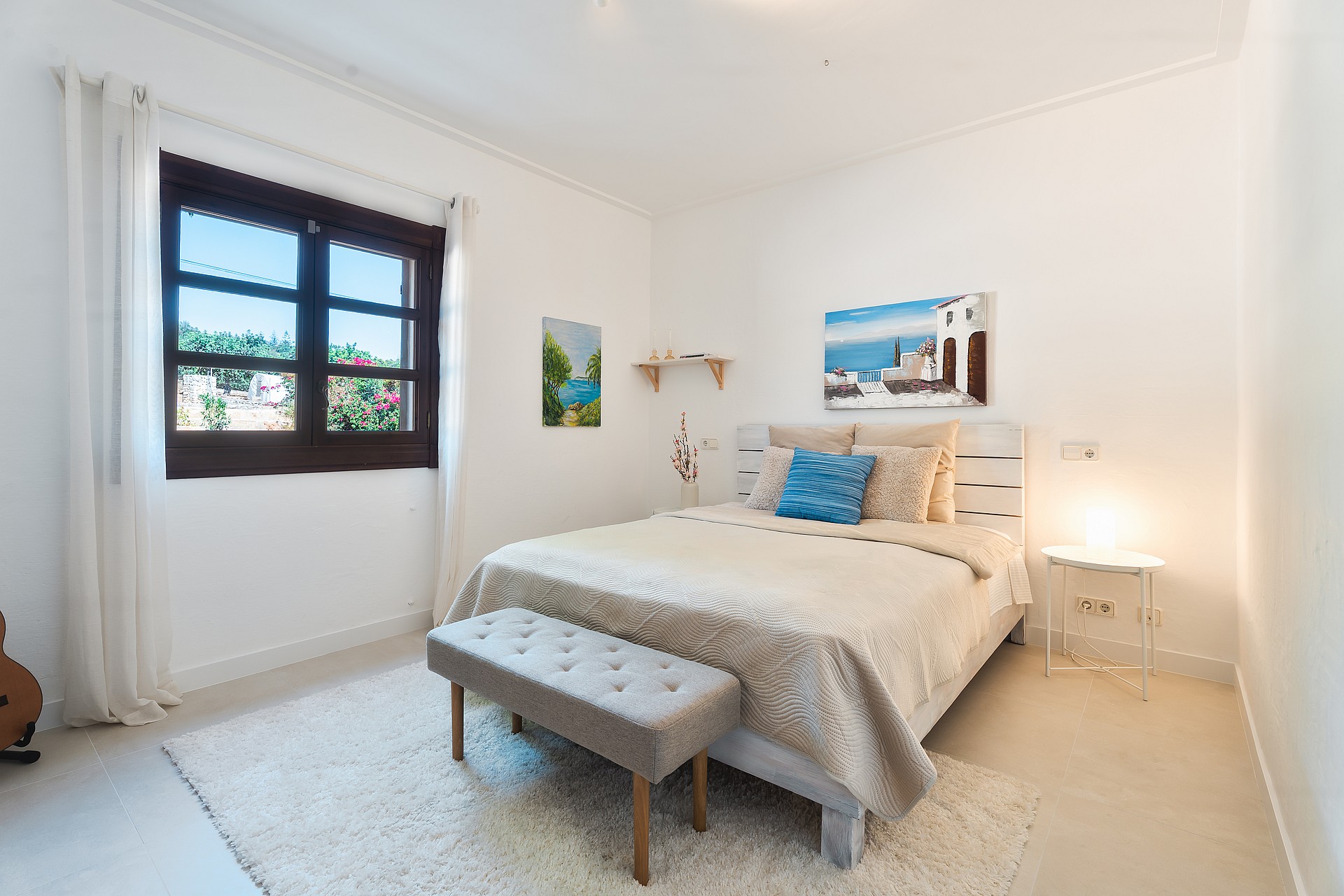 Dormitorio con cama de matrimonio, alfombra de texturas y marco de ventana de madera oscura hacia el verde.