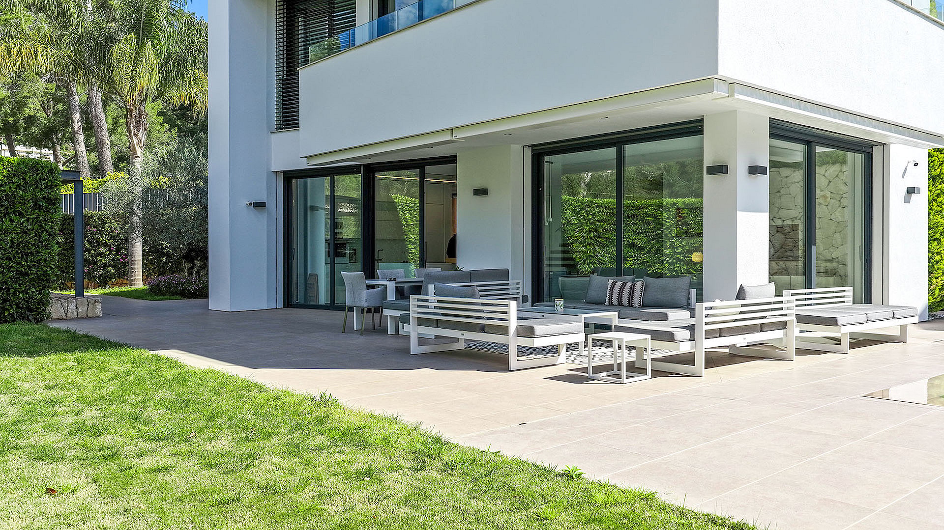 Rear of the villa with covered terrace, outdoor lounge seating and landscaped lawn.