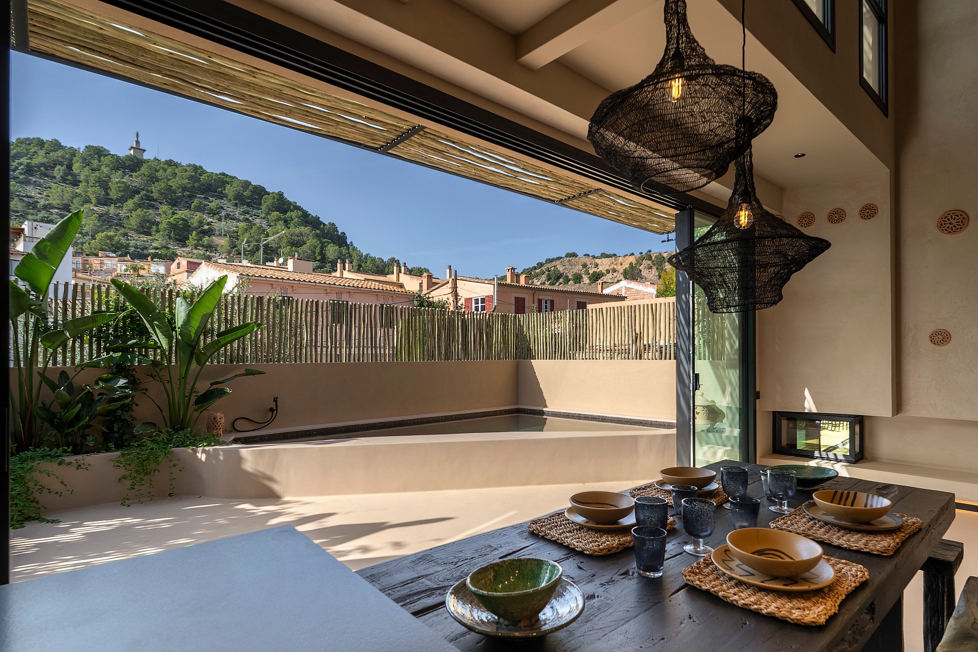 Dining room with large sliding doors opening to an outdoor terrace with a pool, overlooking a hillside.