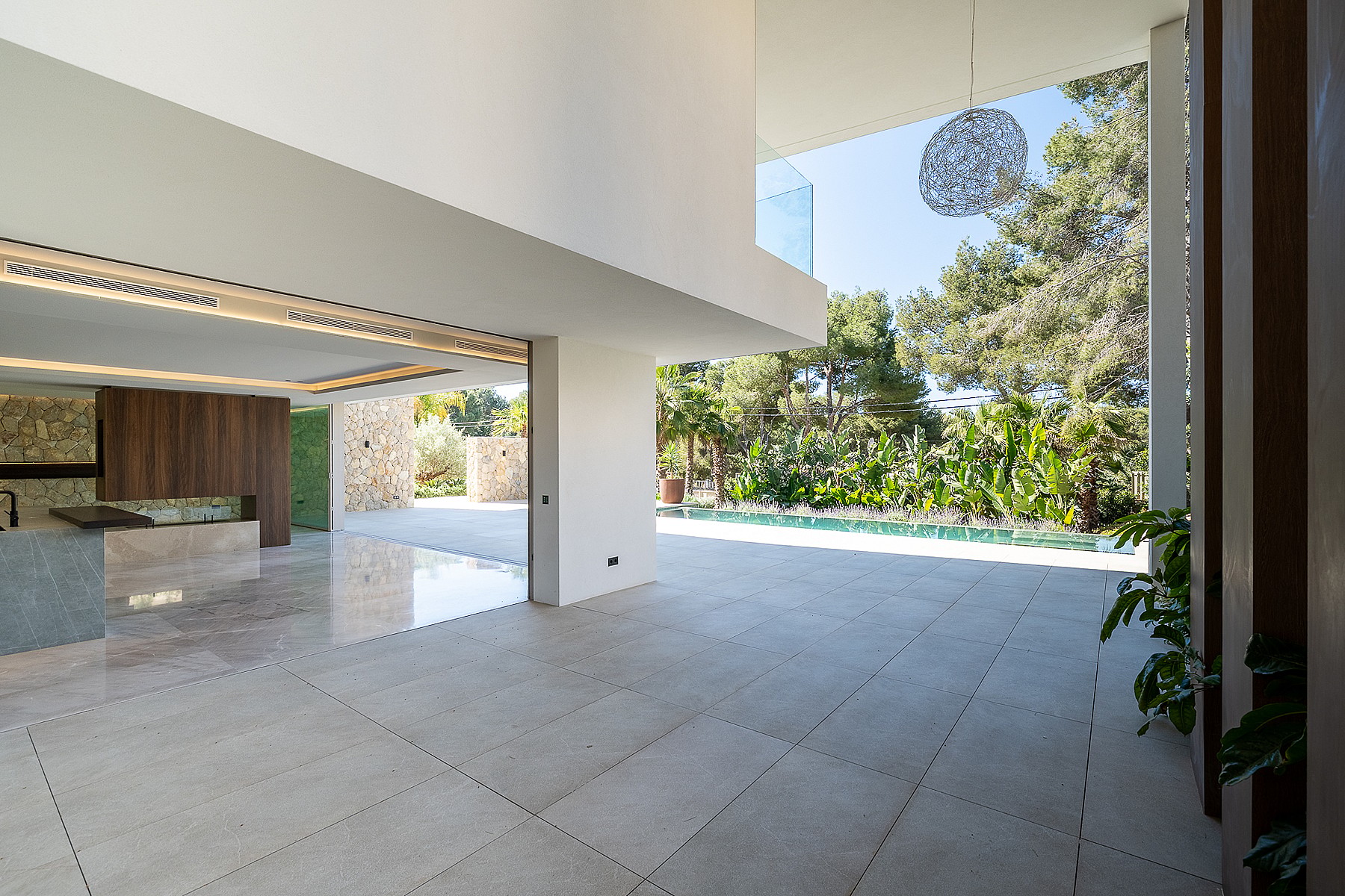 Interior view of a contemporary living area with large floor-to-ceiling glass doors opening onto a sunlit pool terrace.