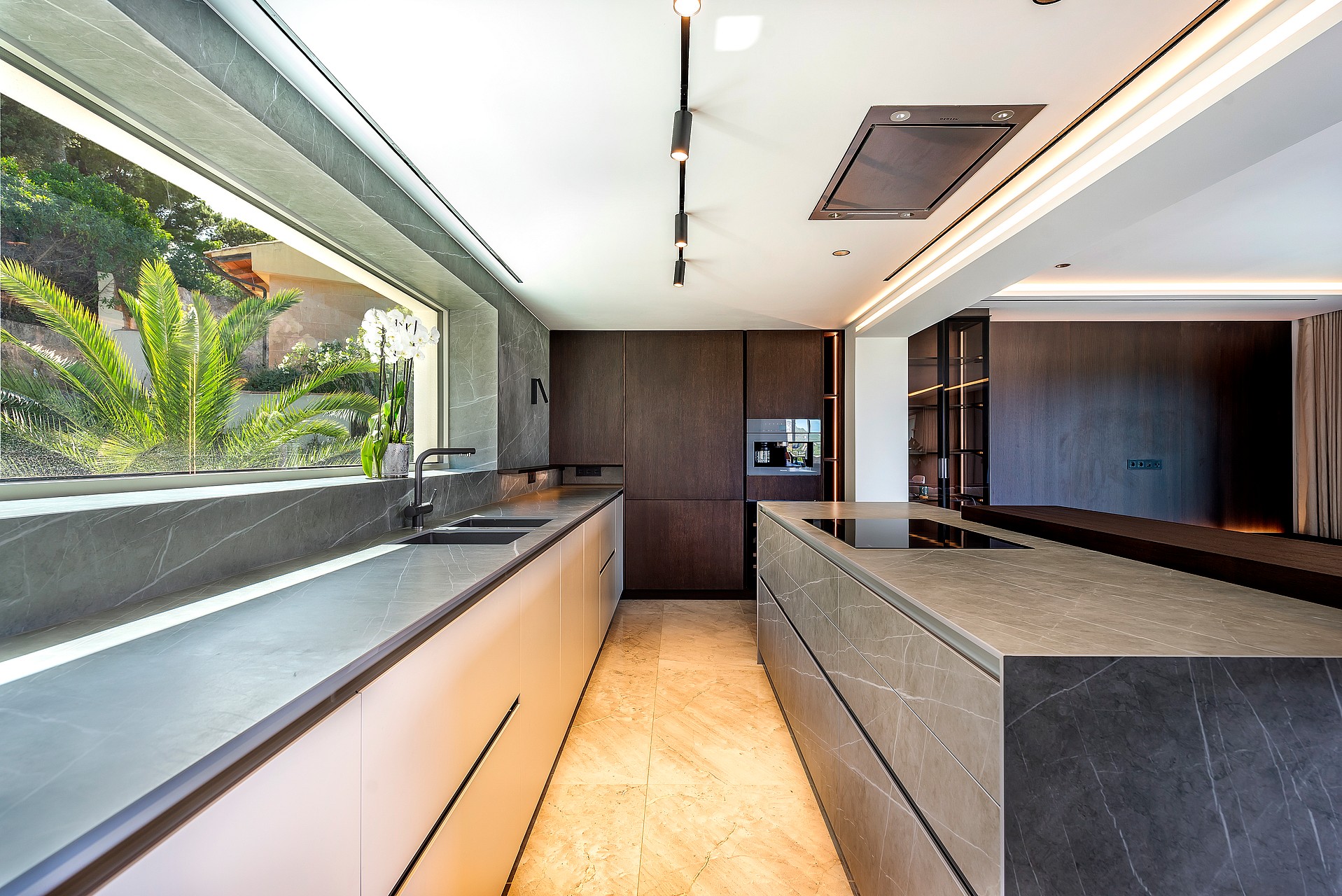 Modern open-plan kitchen featuring a large stone-topped island, dark wood cabinetry, and recessed ceiling track lighting.