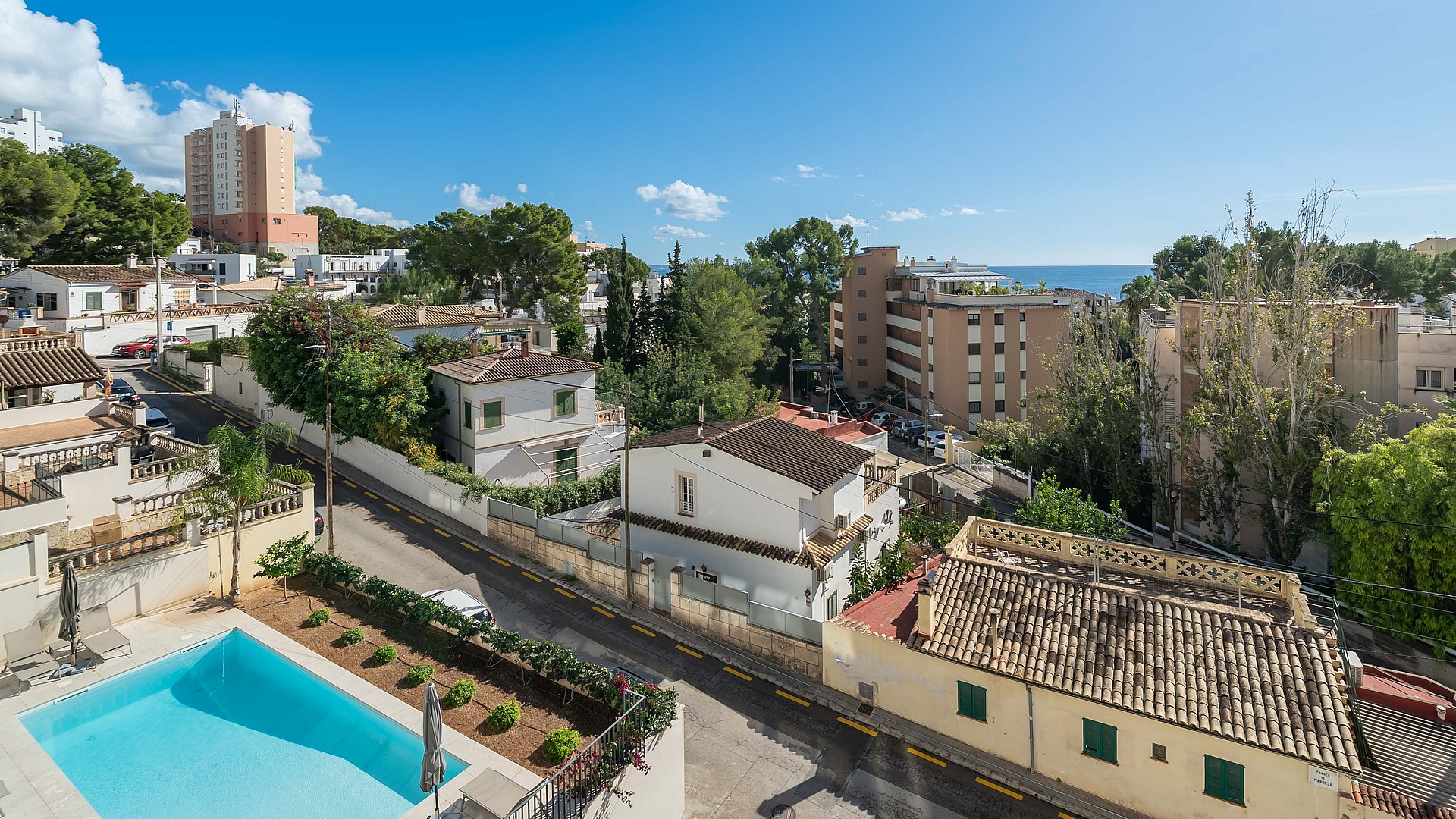 High-angle view of a rectangular outdoor swimming pool with blue water and surrounding residential buildings in a coastal area.
