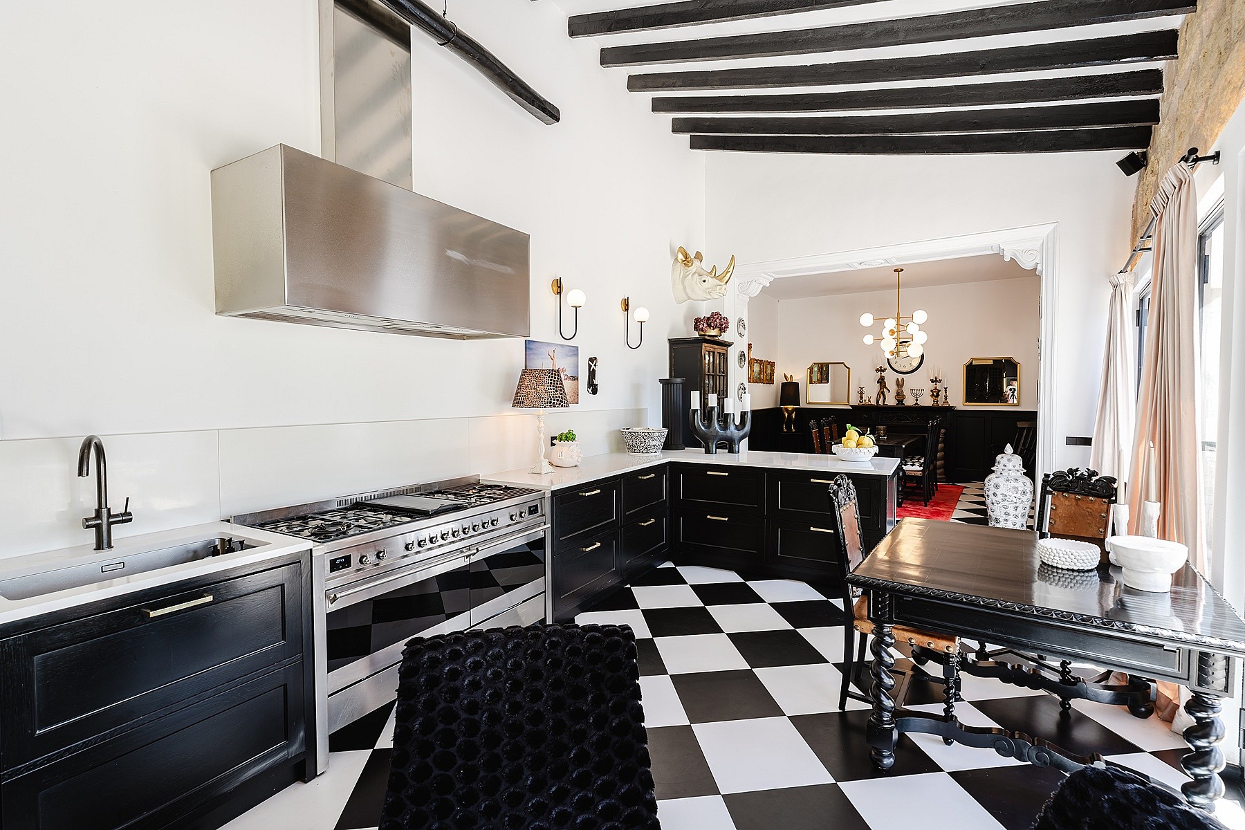 Kitchen features black and white checkered tile floors, black cabinets, a stainless steel range, and exposed dark wood beams.
