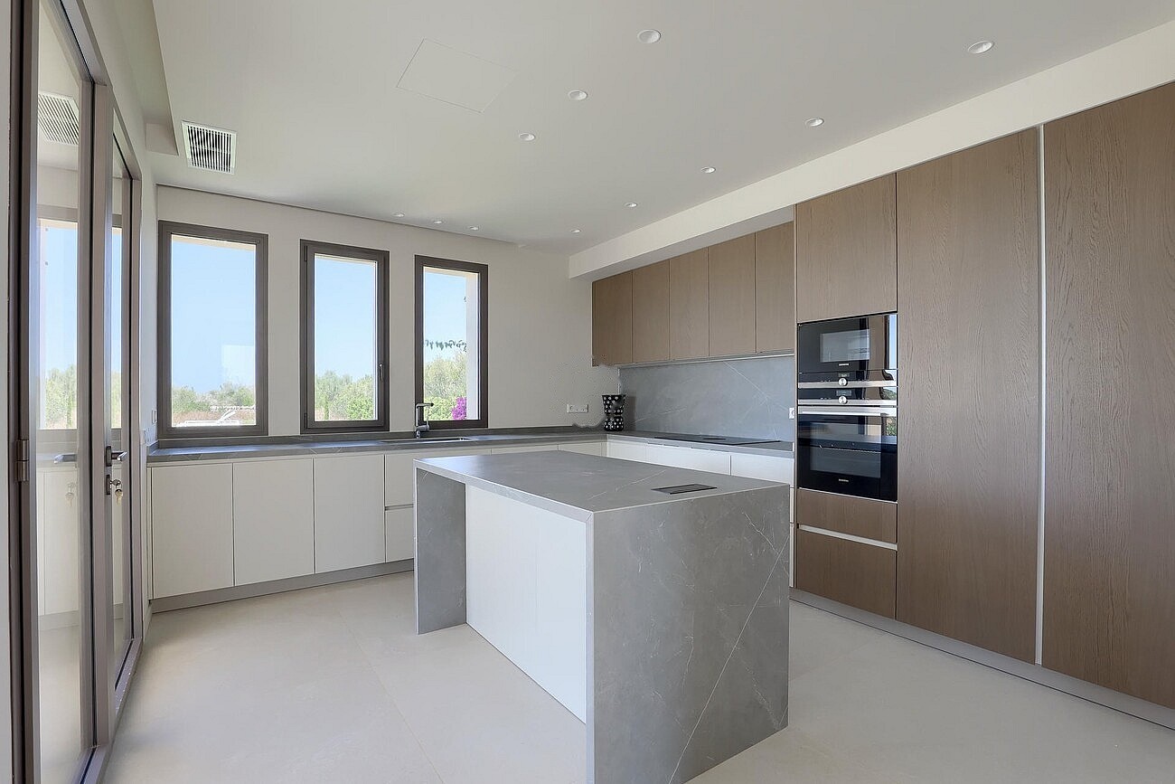Modern kitchen featuring a grey stone island, wood-veneer cabinetry, and white countertops against a neutral wall backdrop.