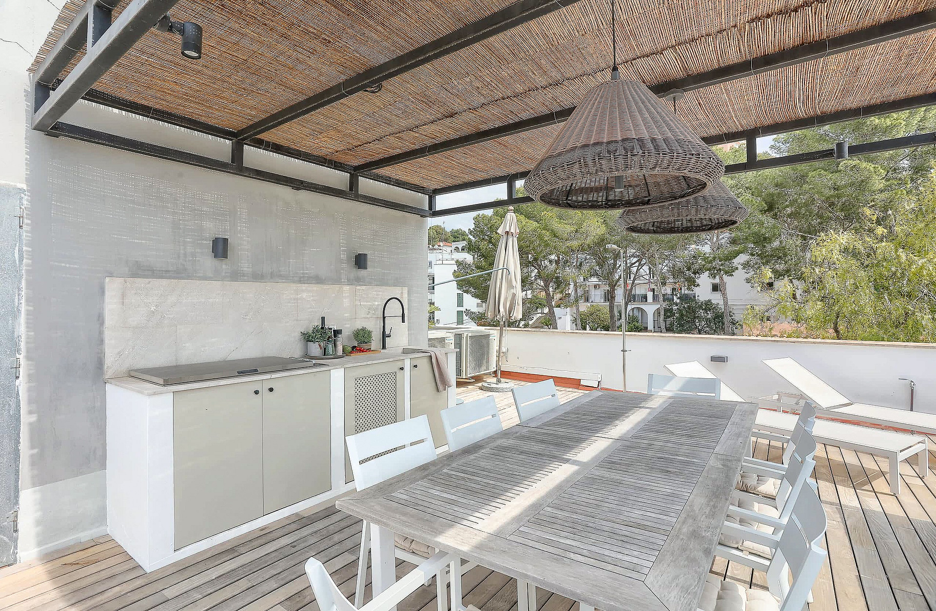 Covered outdoor terrace featuring a built-in kitchenette, dining table with seating, and wooden decking under a pergola.