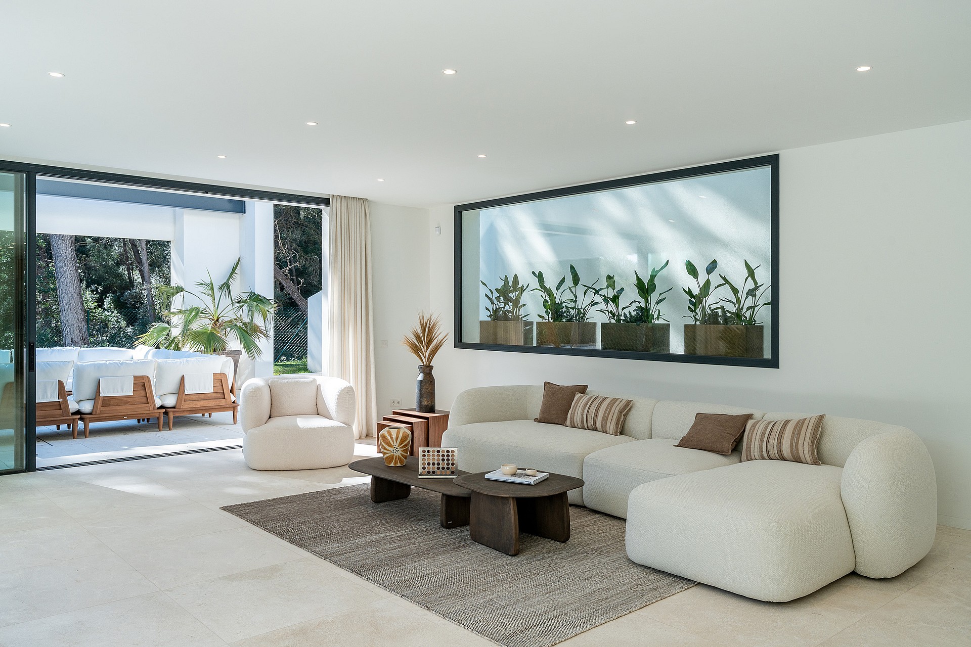 Spacious open-plan living room with bouclé sofas, stone flooring and floor-to-ceiling sliding doors opening to the pool terrace