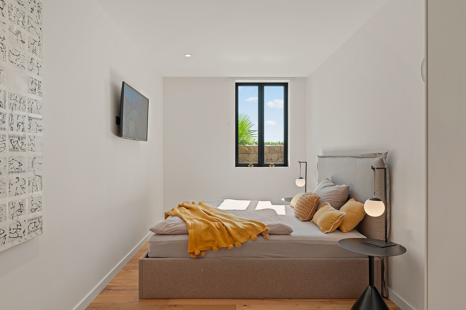 A modern bedroom featuring a bed with a grey upholstered headboard, a golden-yellow throw blanket, and a minimalist side table.