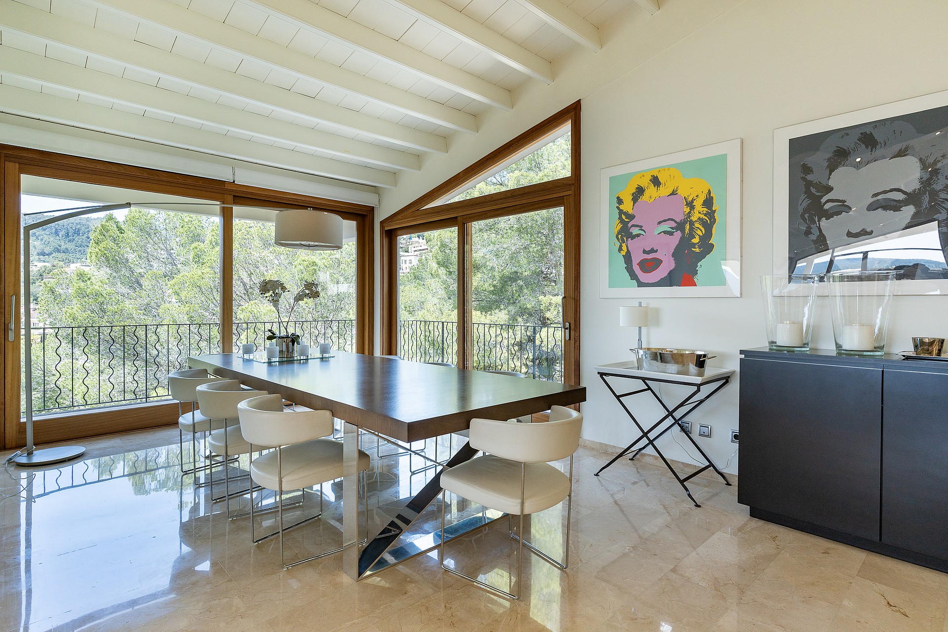 Large open-plan reception room with white beam ceilings, marble floors and art-hung wall leading to dining area