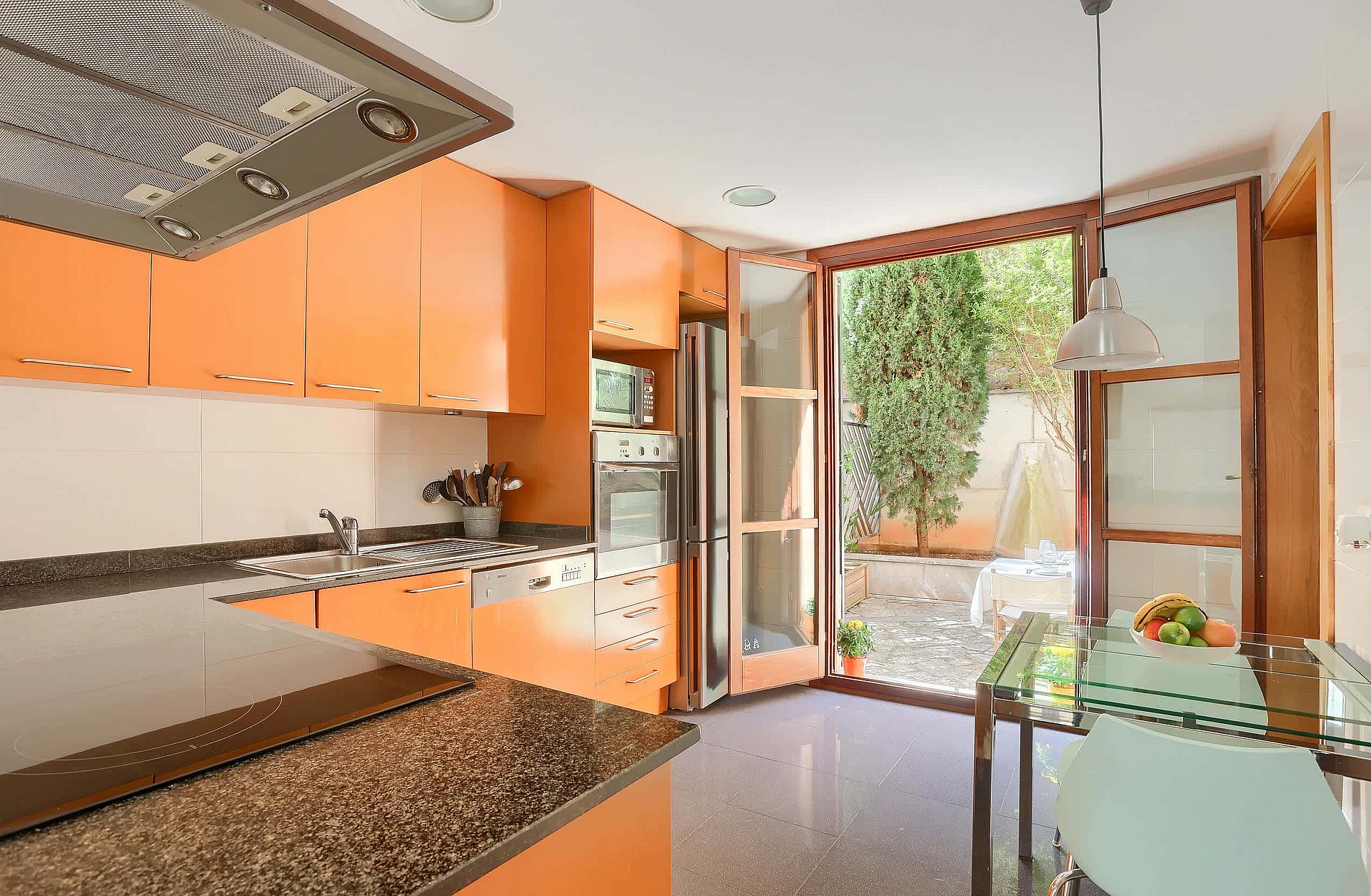 Modern kitchen with orange cabinetry, granite countertops, and glass door leading to a private outdoor garden area.