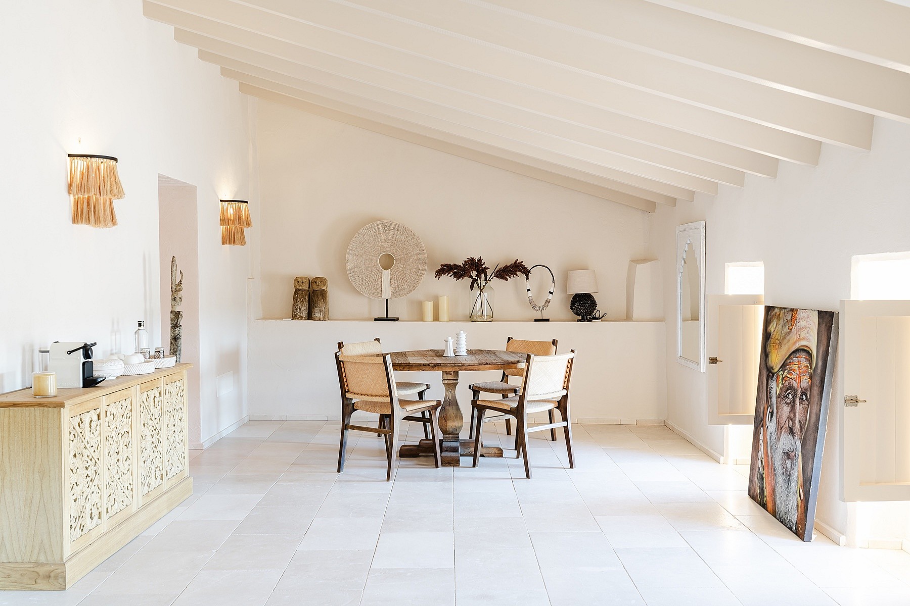 Dining room featuring a round wooden table, white stone floors, and a vaulted ceiling with exposed white-painted beams.