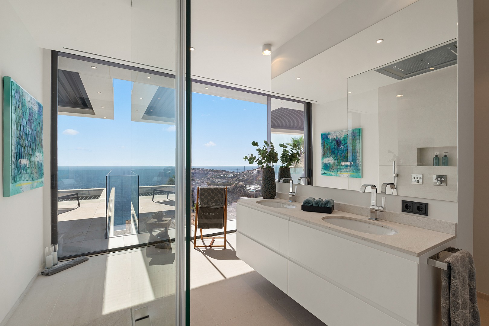Modern bathroom featuring a double vanity, large mirror, and expansive window overlooking the sea.