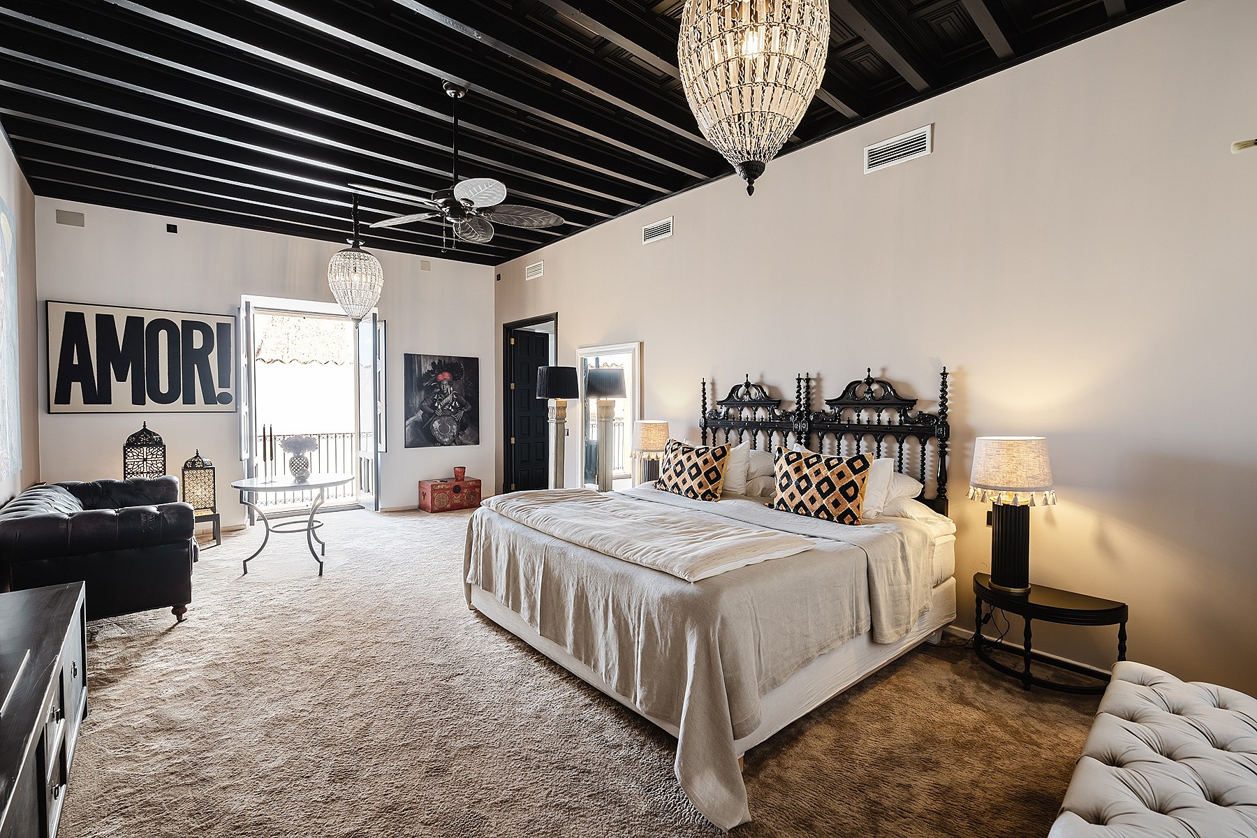A spacious master bedroom in a Sencelles townhouse featuring a black exposed beam ceiling, a wrought iron bed, and neutral walls.