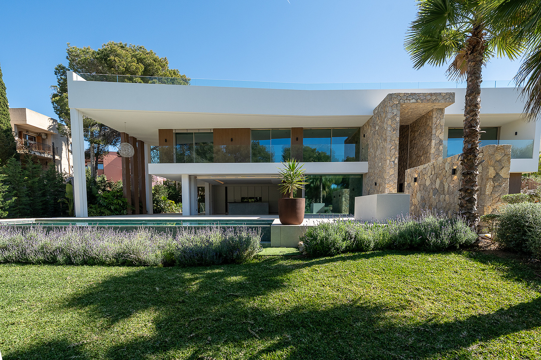 Exterior view of a two-story modern villa in Santa Ponsa featuring white plaster, natural stone walls, and a swimming pool.