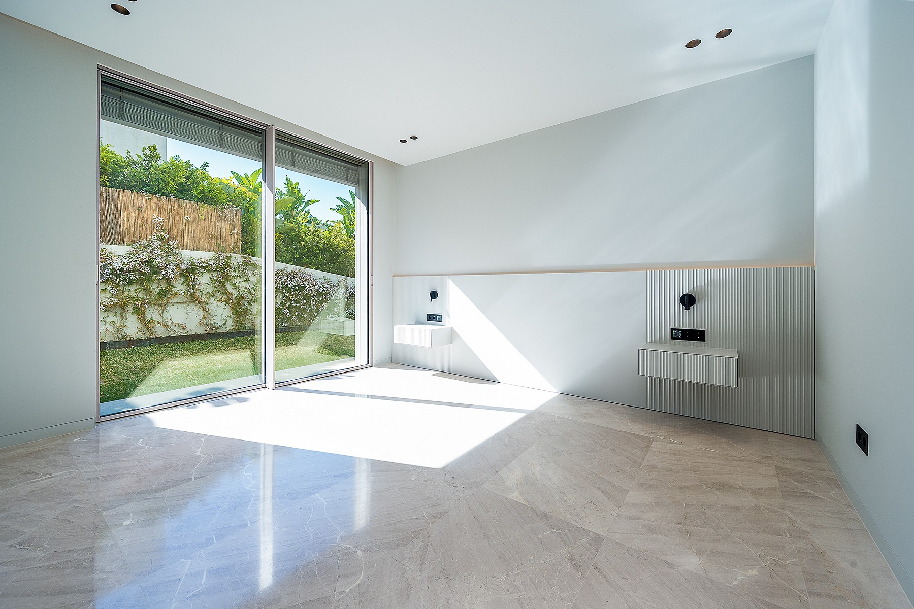 A modern bathroom featuring polished stone flooring, two floating vanity basins, and large sliding glass doors opening to a garden.
