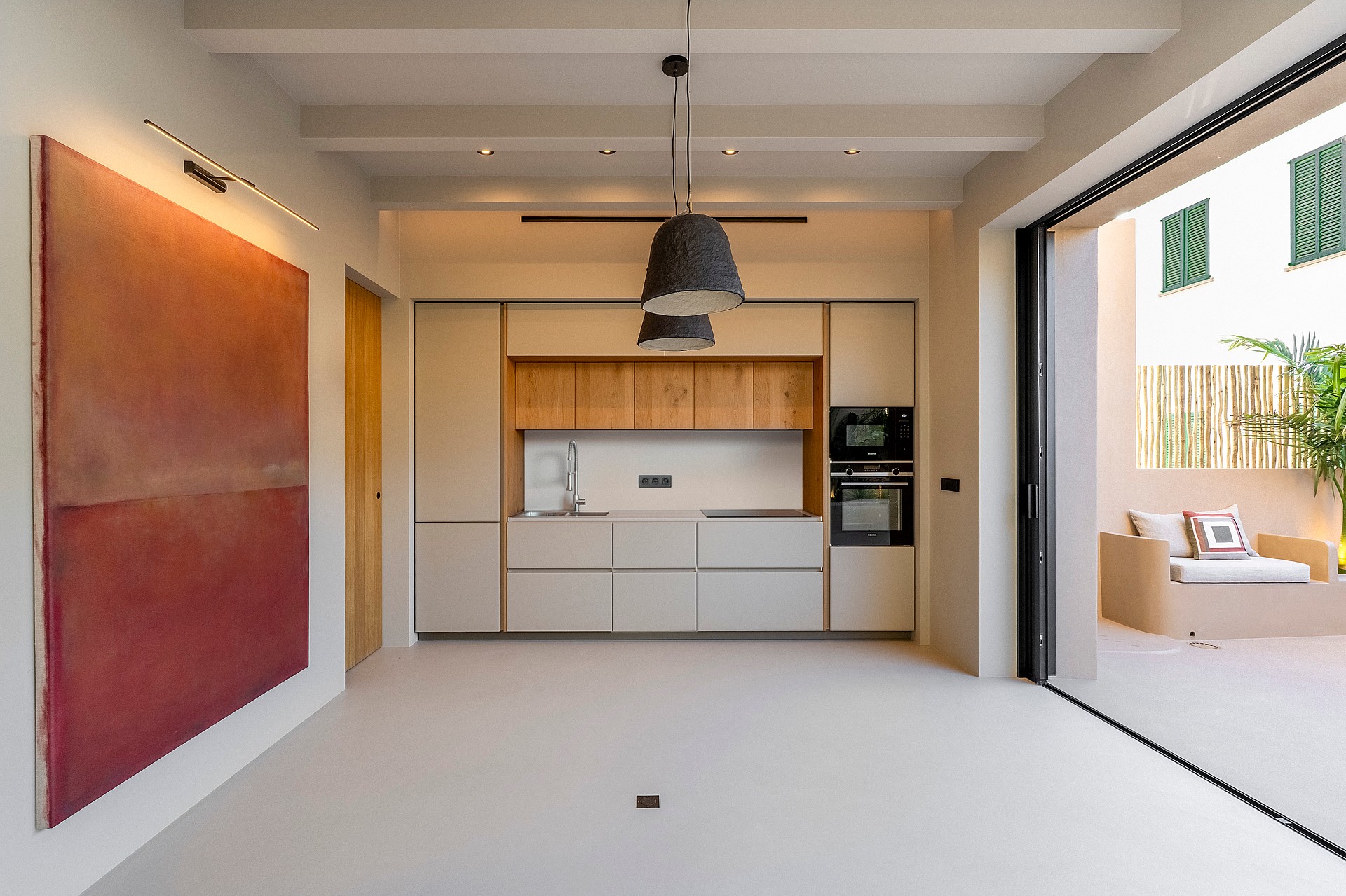 Modern kitchen with white and oak cabinetry, micro-cement floors, and sliding glass doors leading to a sun-drenched terrace.