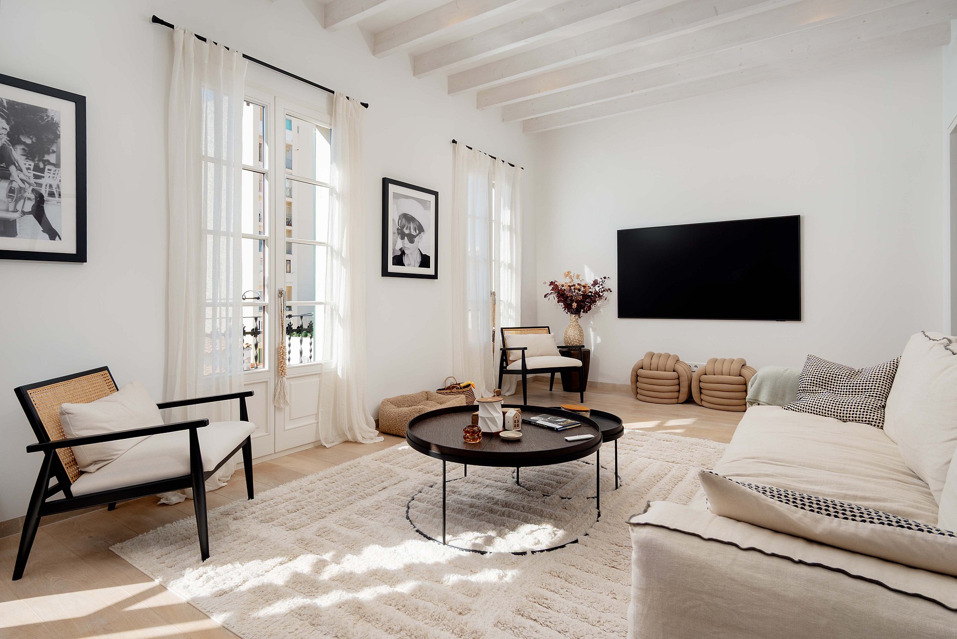 A bright living room in Santa Catalina with white walls, exposed white wooden ceiling beams, and French doors with linen curtains.