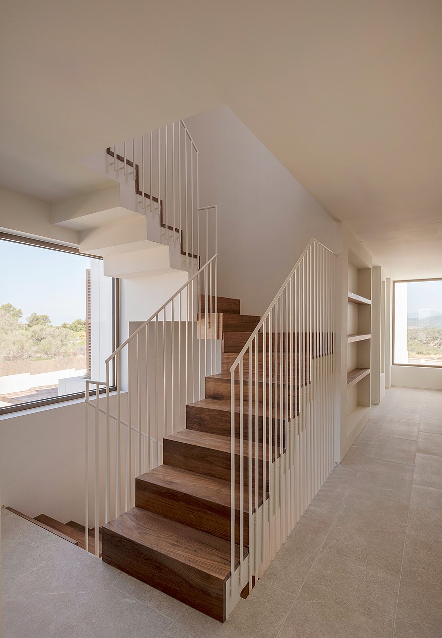 A staircase with dark wood treads and a white metal spindle railing, set against white walls with a large window.